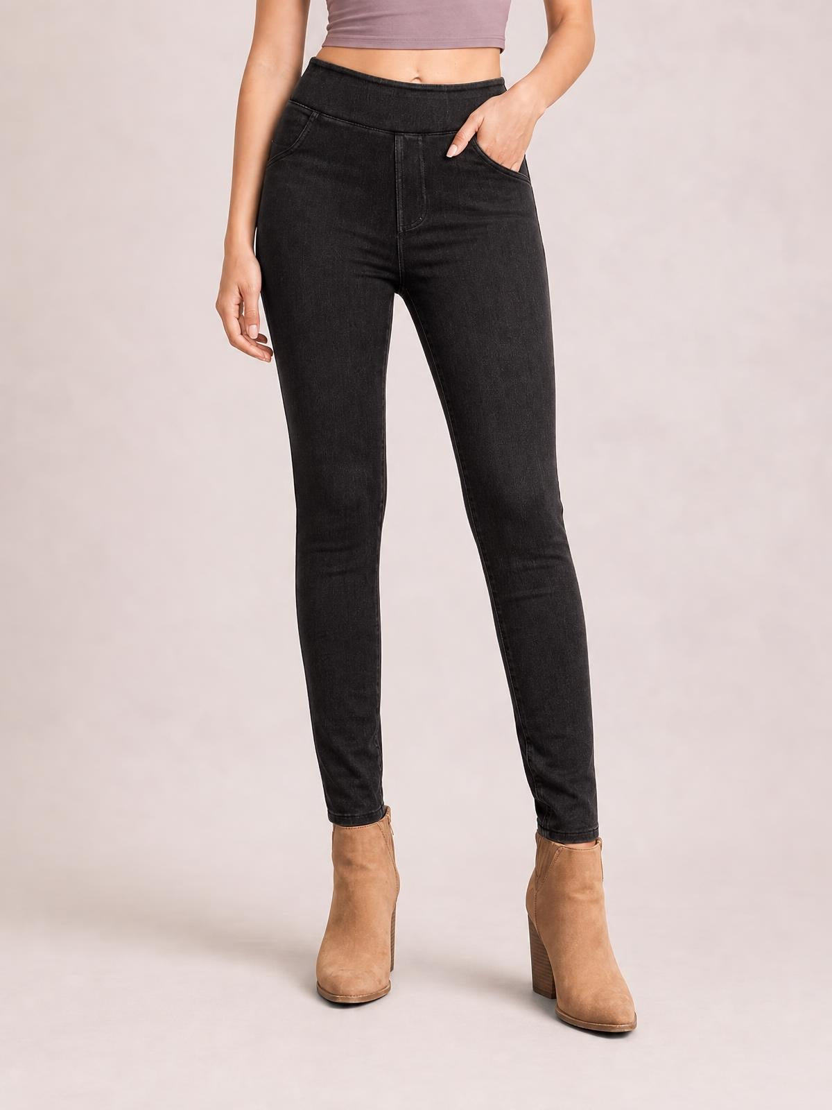Model wearing black skinny jeans with front pockets, a high-rise waistband, fitted silhouette, and tapered legs, standing with one hand in a pocket.