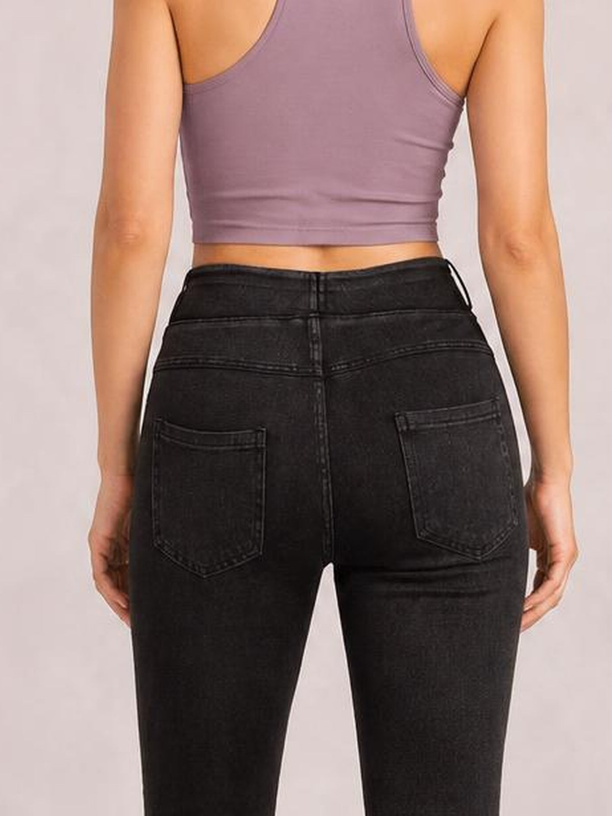 Model shown from the back wearing black skinny jeans with stitched waistband, center seams, and two visible back pockets in a fitted silhouette.