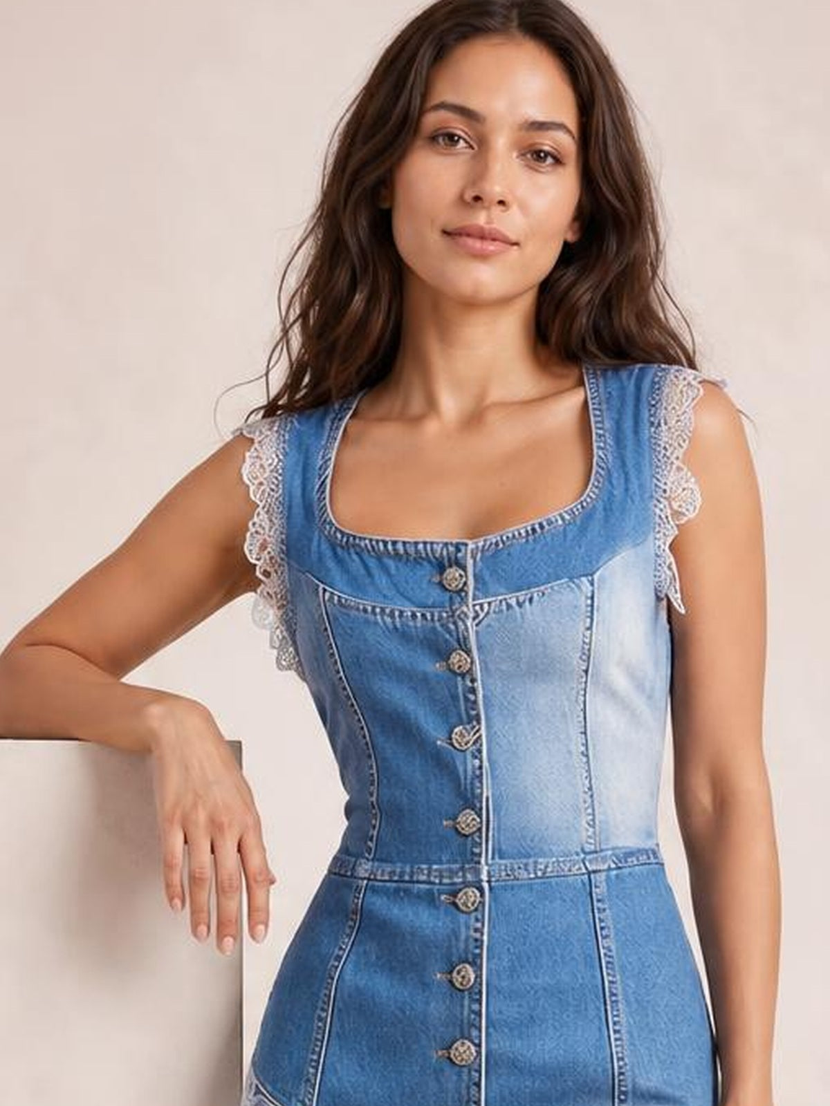 A woman poses in a blue sleeveless patchwork denim dress with a square neckline, buttoned front, fitted silhouette, and lace-trimmed shoulder edges.