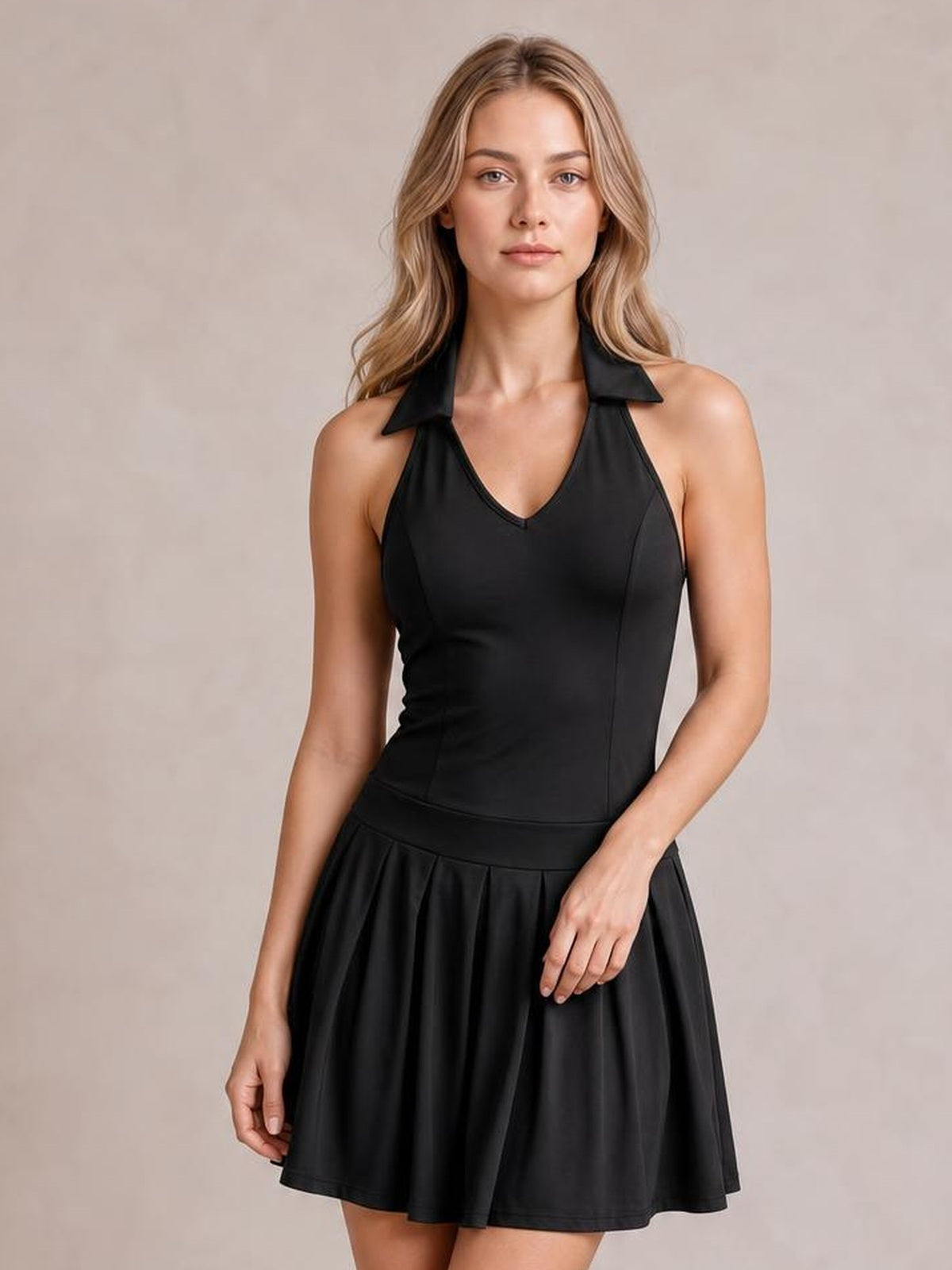 Model wearing a black sleeveless pleated active dress with a fitted V-neck bodice, collar detail, defined waist seam, and flared skirt.