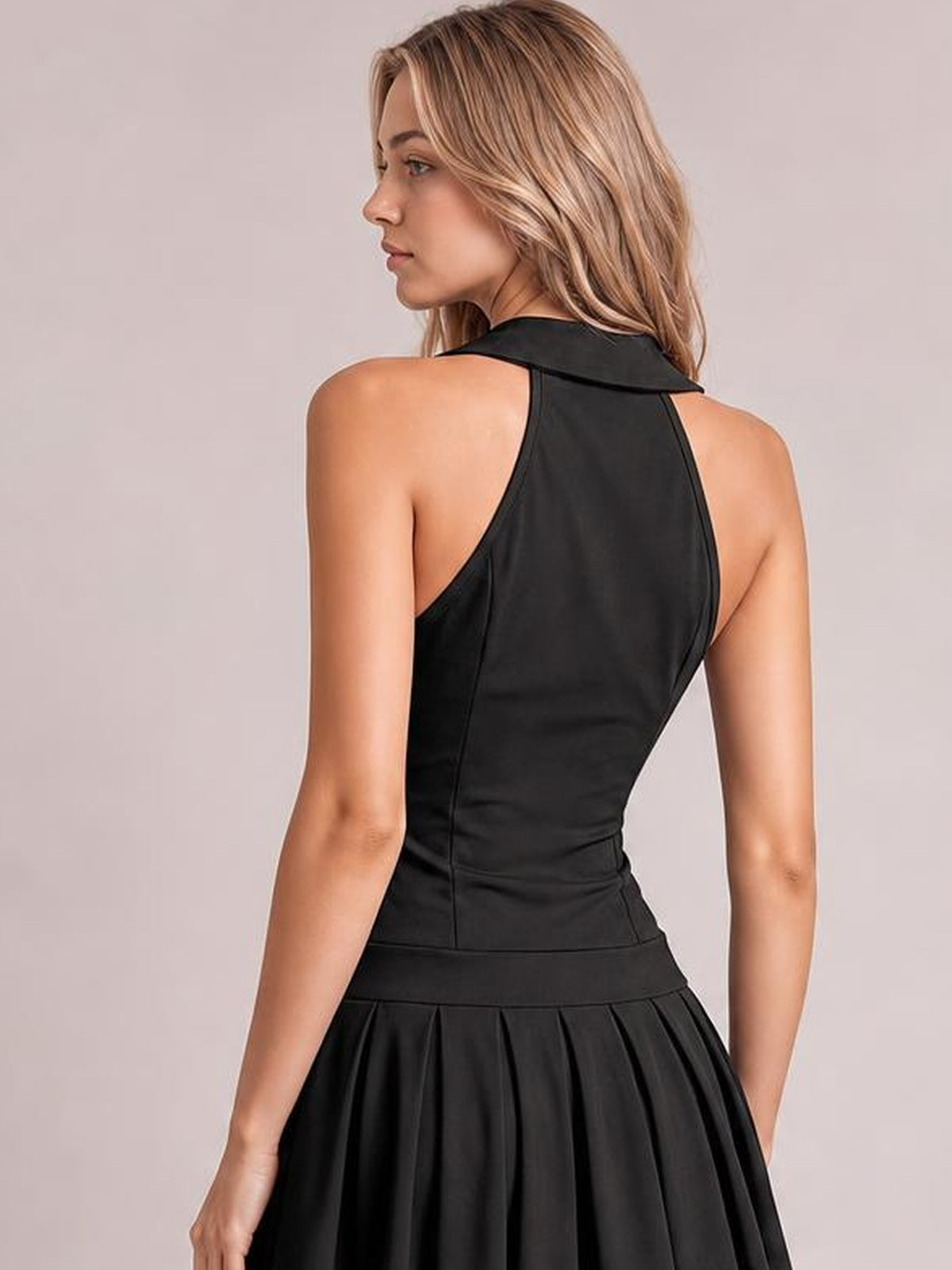 Model shown from the back in a black sleeveless active dress with a fitted bodice, high neckline, seamed construction, and pleated flared skirt.