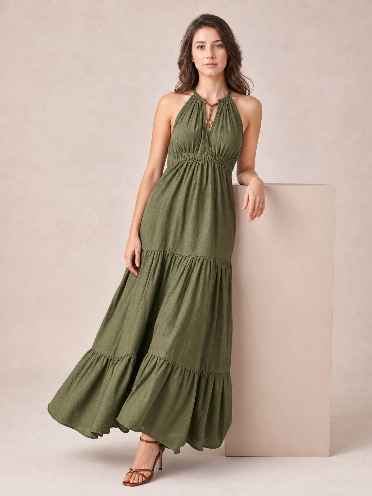 A model poses in an olive green sleeveless halter maxi dress with a keyhole neckline, smocked waist, and flowing tiered skirt.
