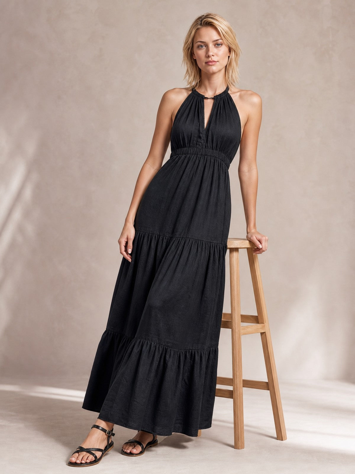 A model poses in a black sleeveless tiered maxi dress with a halter neckline, keyhole detail, smocked waist, and flowing floor-length silhouette.