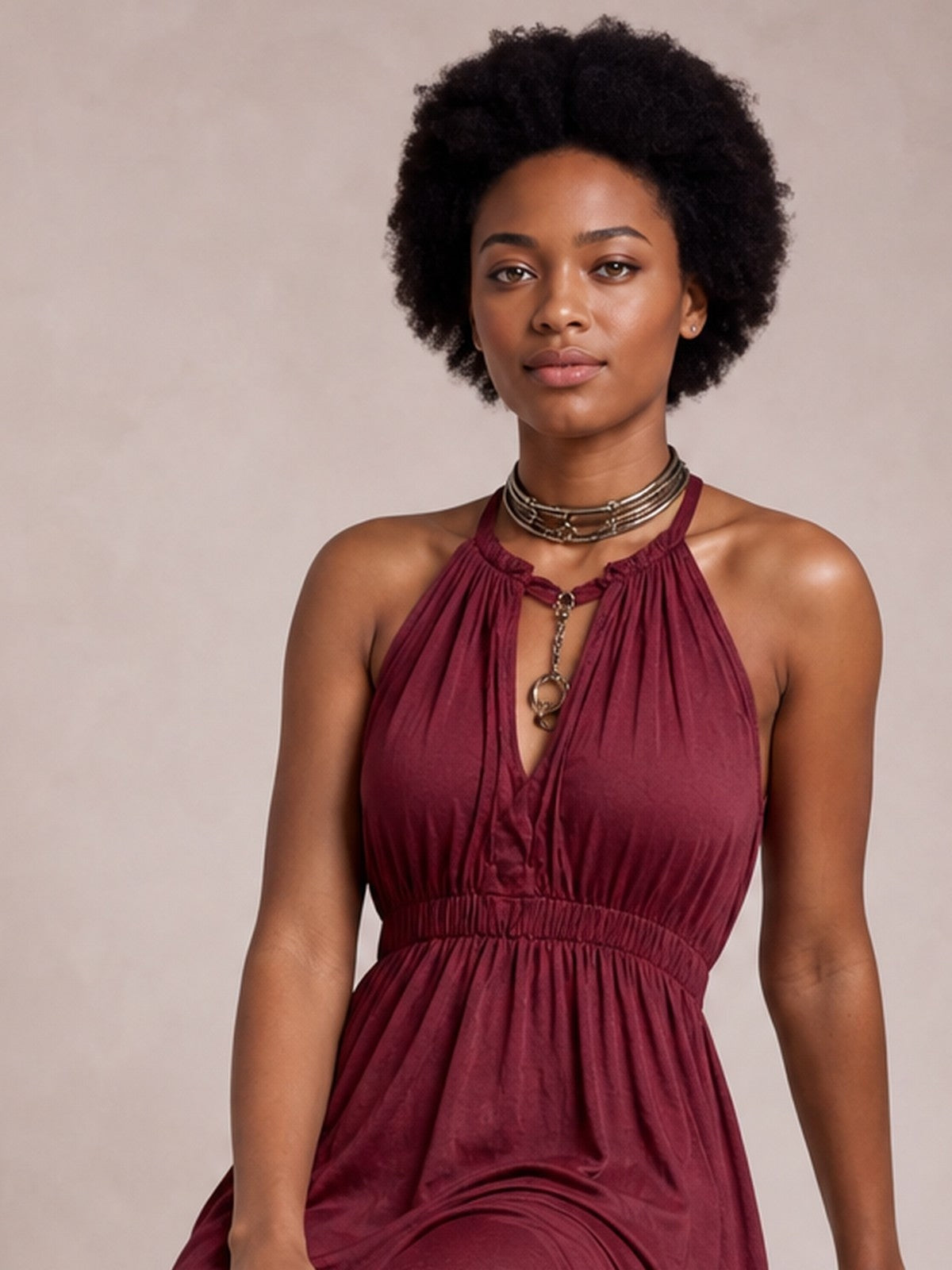 A model stands with her arms at her sides in a burgundy sleeveless halter maxi dress with a keyhole neckline, gathered bodice, smocked waist, and flowing skirt.