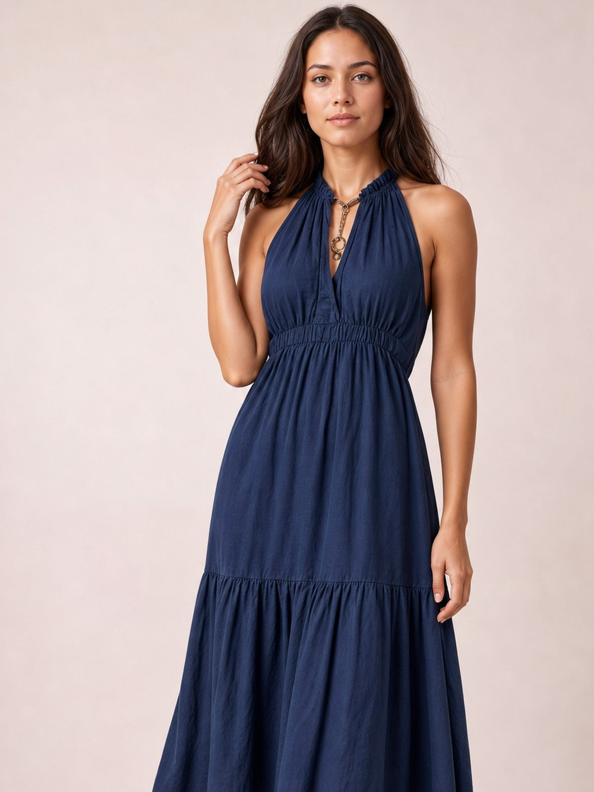 Model poses in a navy sleeveless tiered maxi dress with a halter neckline, keyhole detail, gathered bodice, smocked waist, and flowing skirt.
