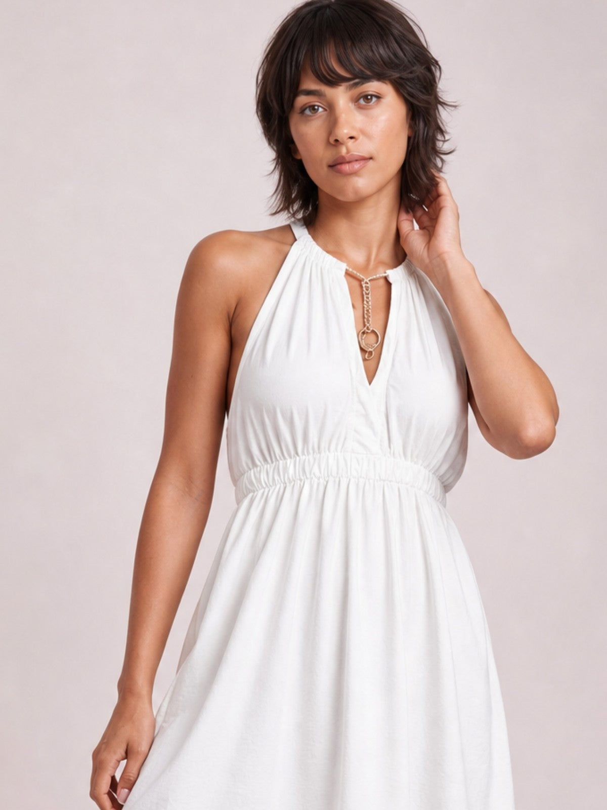 A model poses in a white sleeveless maxi dress with a halter neckline, gathered bodice, smocked waist, and flowing full skirt.