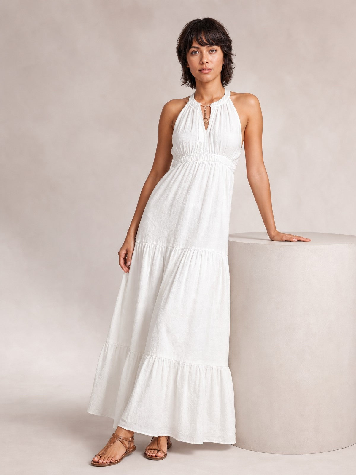 A model stands in a white sleeveless halter maxi dress with a keyhole neckline, gathered bodice, smocked waist, and flowing tiered skirt.