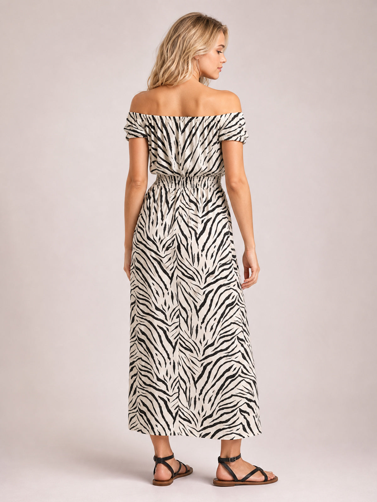 Model shown from behind in a white and black animal-print midi dress with an off-shoulder neckline, short sleeves, gathered waist, and flowing silhouette.