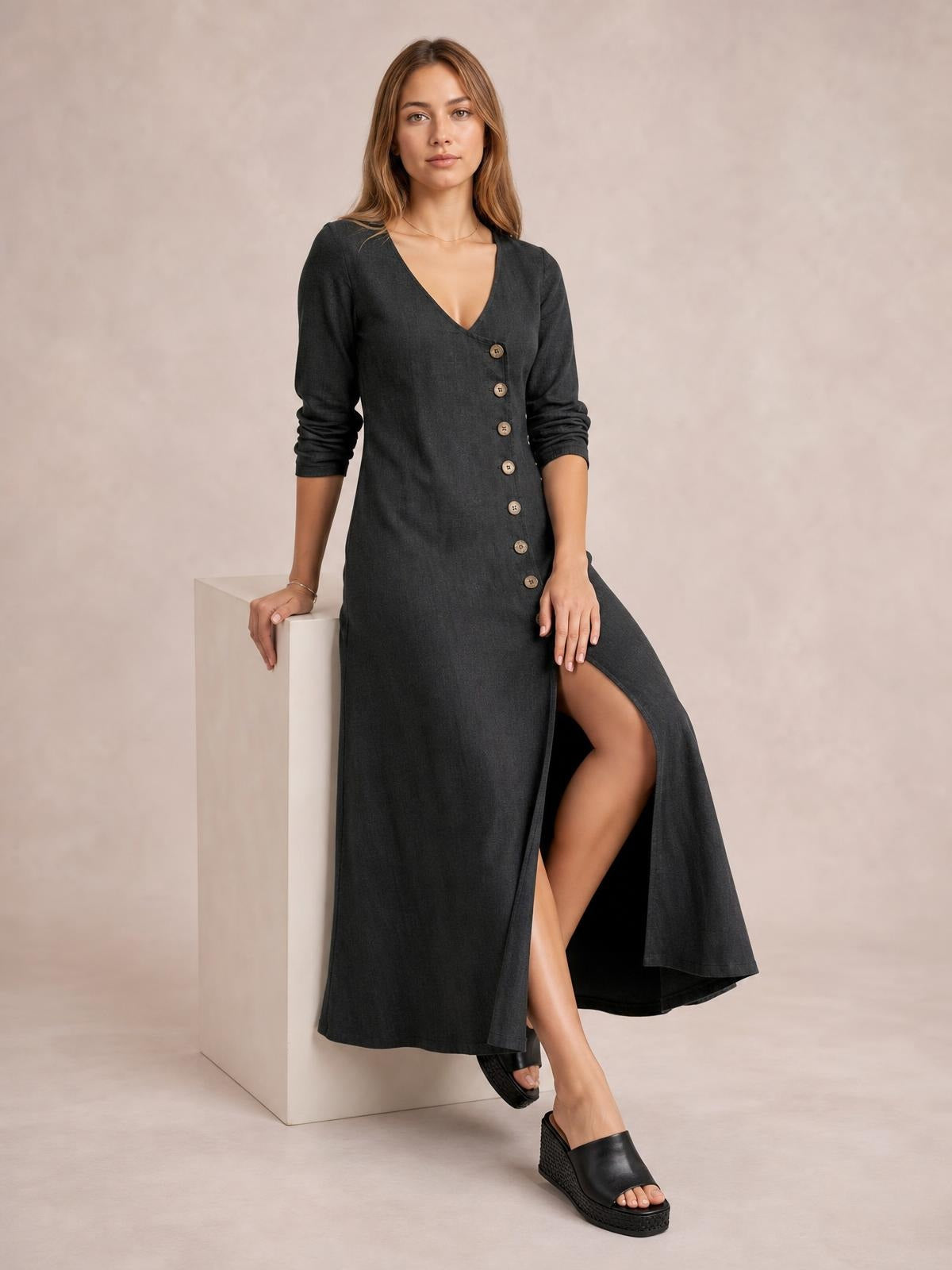 Model poses in a charcoal button-down midi dress with long sleeves, a V-neckline, diagonal buttons, and a flowing side slit.