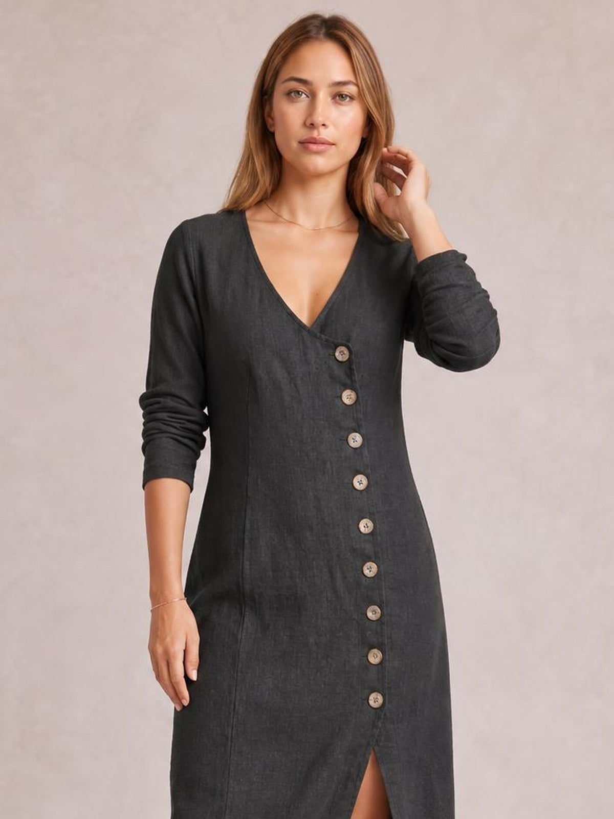 Model poses in a charcoal midi dress with a V-neck, long sleeves, button-down front, fitted silhouette, and front slit.