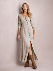 Model standing in a beige button-down midi dress with long sleeves, a fitted silhouette, V-neckline, front buttons, and a high front slit.