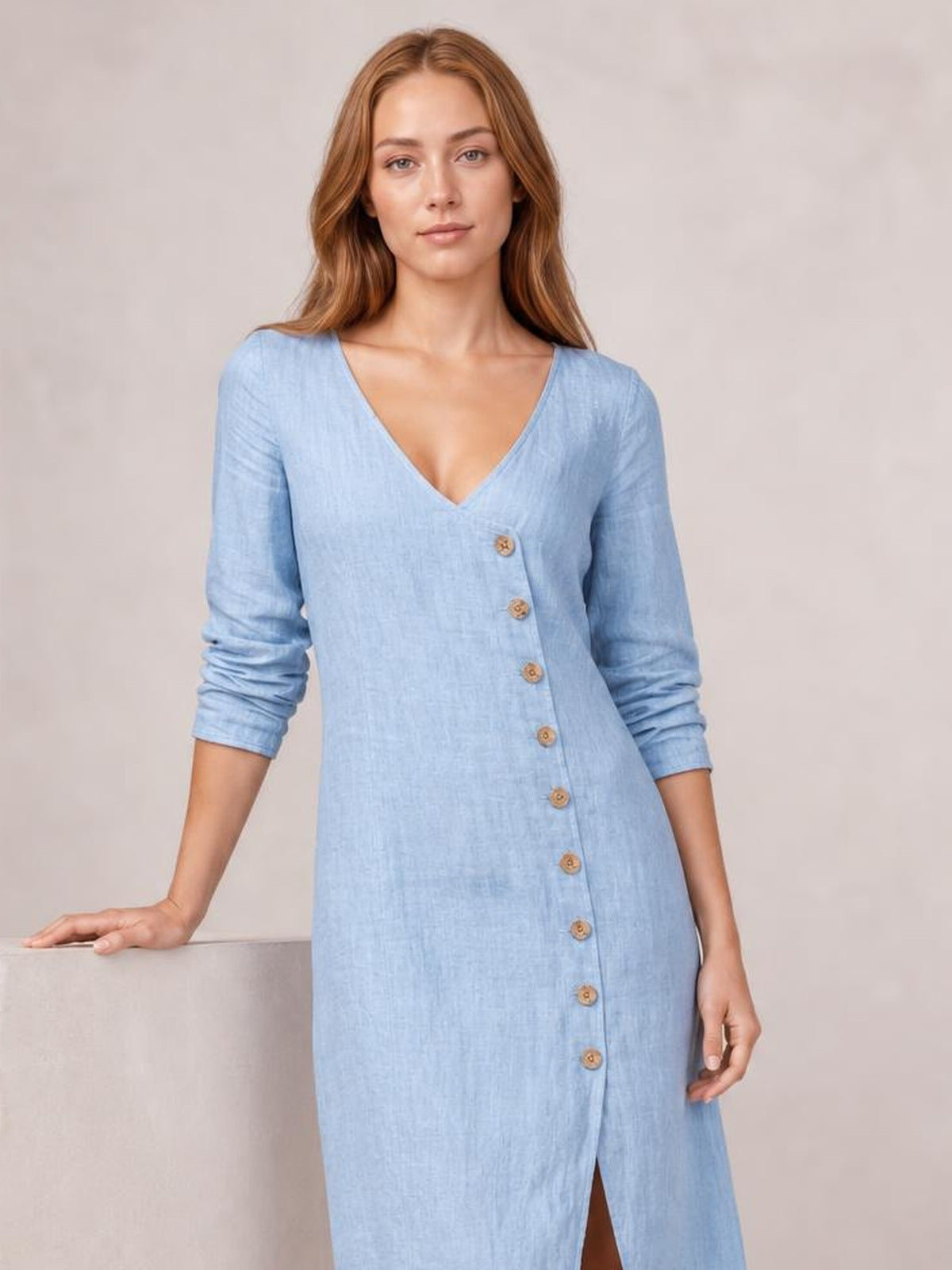 A model wears a light blue button-down midi dress with a V-neck, long sleeves, straight silhouette, front buttons, and a visible hem slit.