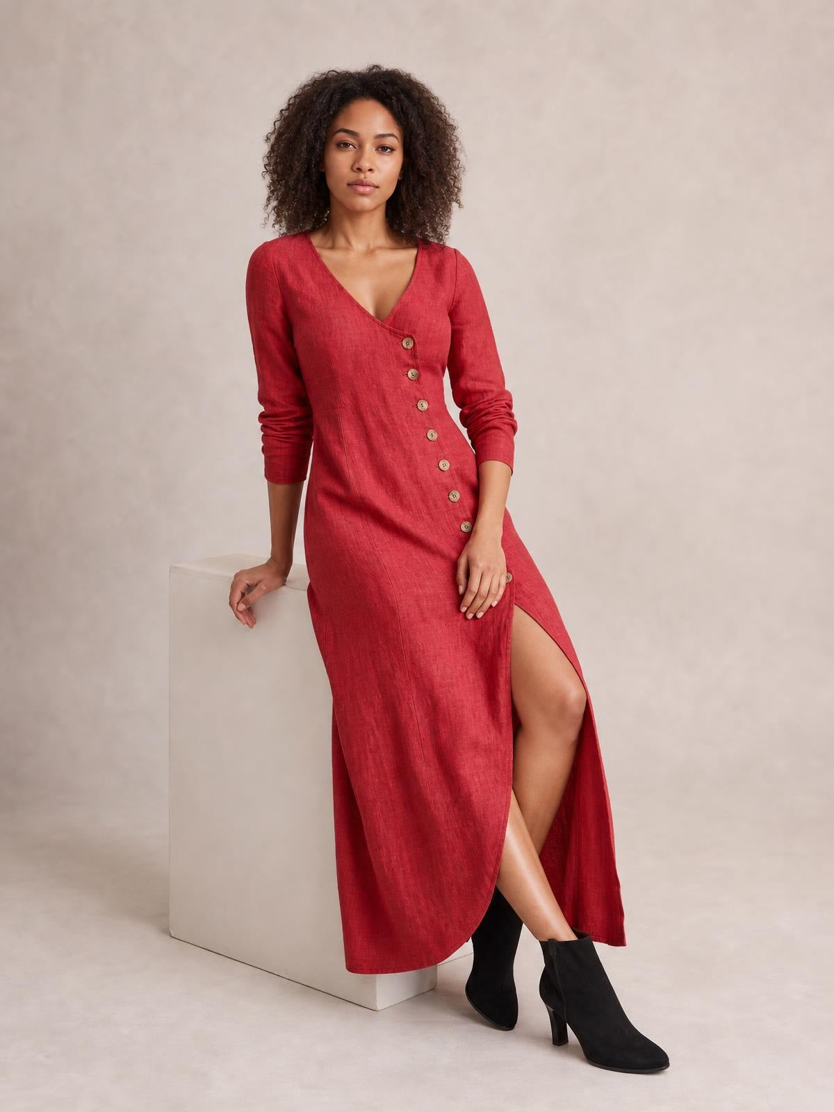 Model seated in a red midi dress with a V-neck, long sleeves, diagonal button-down front, and a high side slit revealing one leg.
