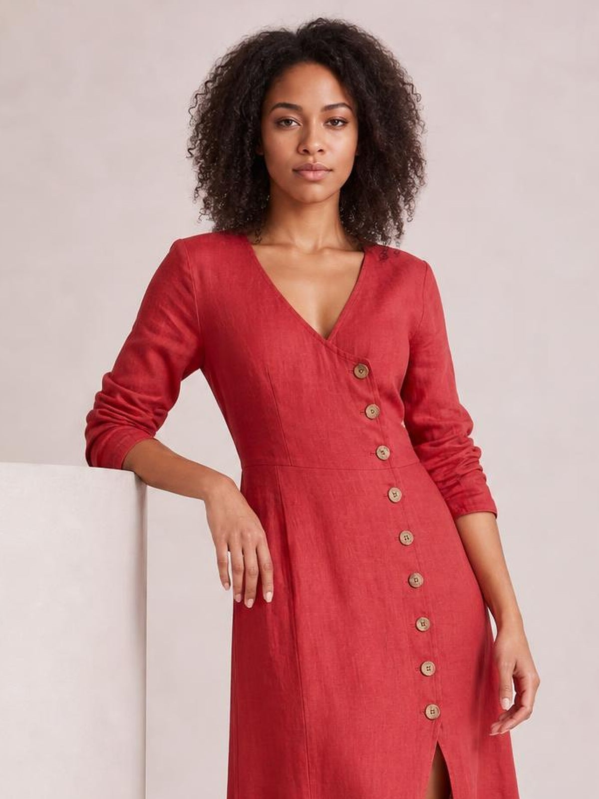 Model in a relaxed pose wears a red midi dress with a V-neck, long sleeves, button-down front, defined waist, and front slit.