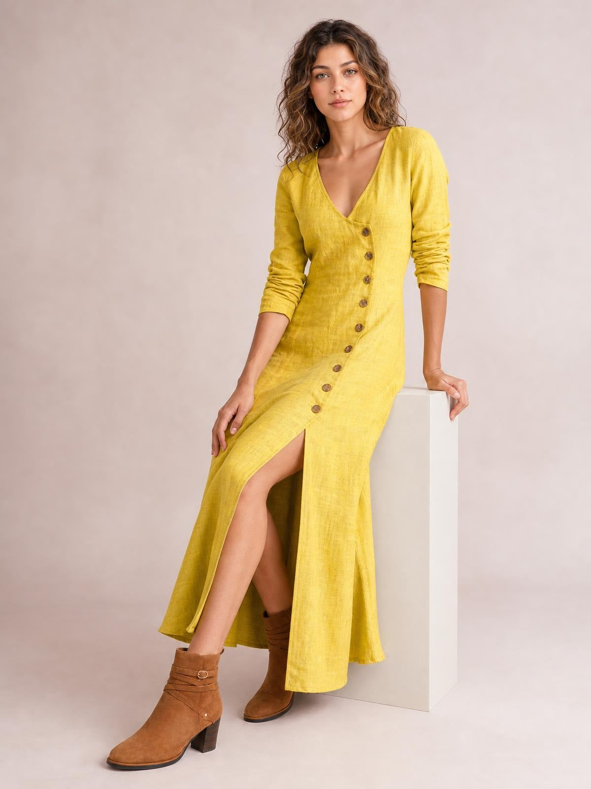 Model seated in a yellow midi dress with a V-neck, long sleeves, front button-down construction, and a high leg slit.