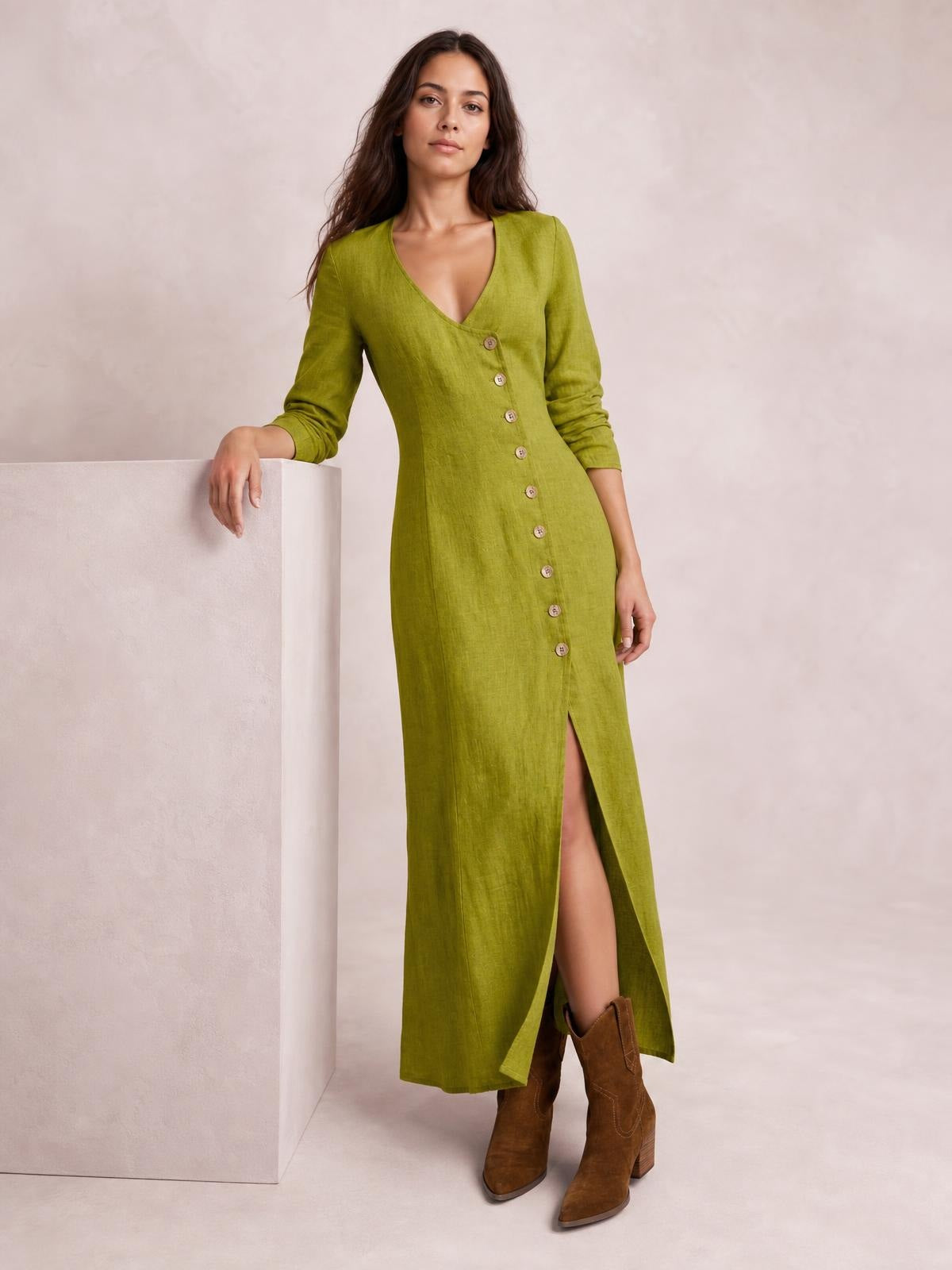 Model wearing an olive green button-down midi dress with long sleeves, a V-neckline, fitted silhouette, and front slit, leaning casually with one hand on a block.