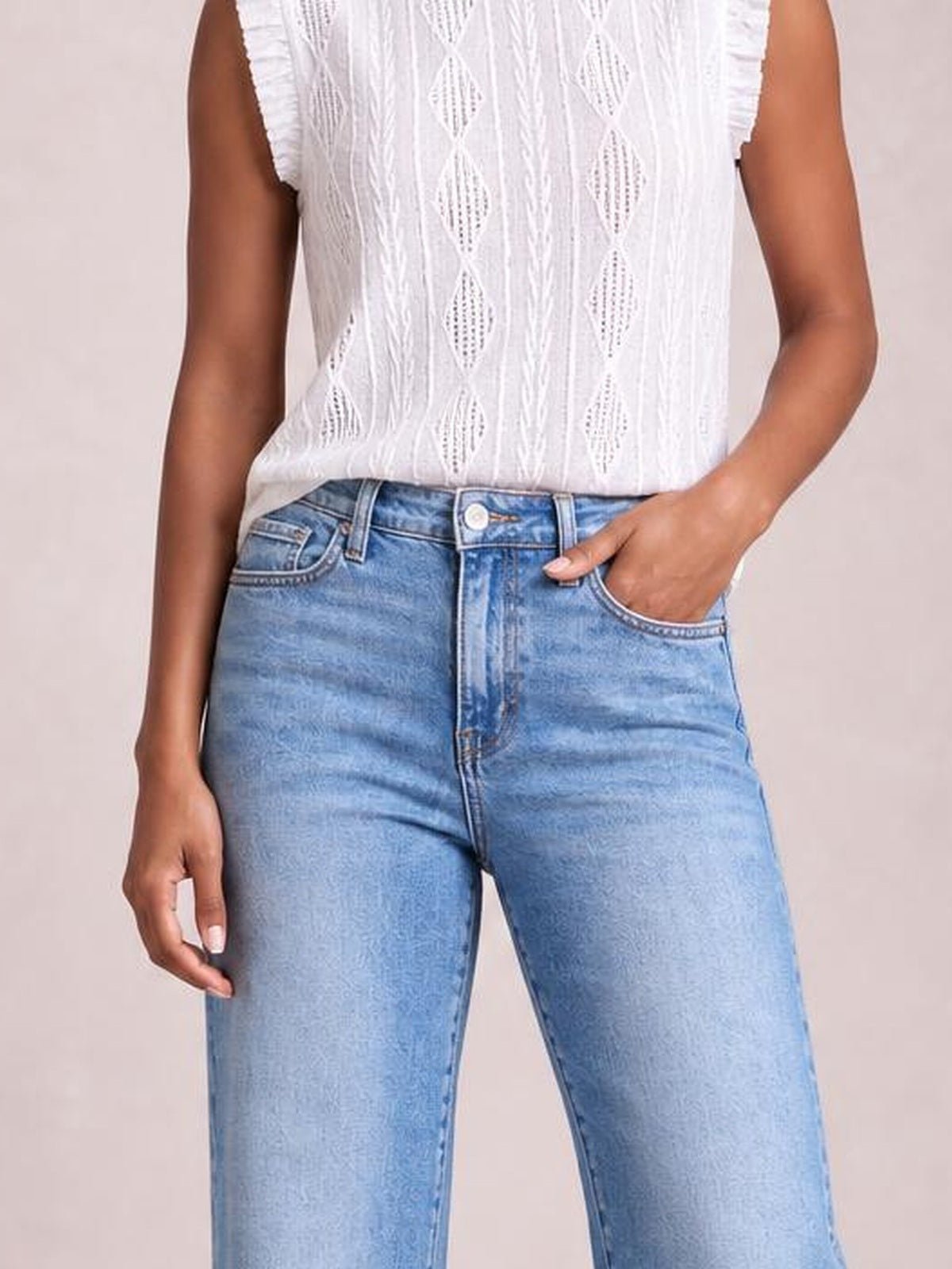 A model wears light blue buttoned jeans with belt loops, curved front pockets, and a relaxed straight-leg silhouette, posing with one hand in a pocket.
