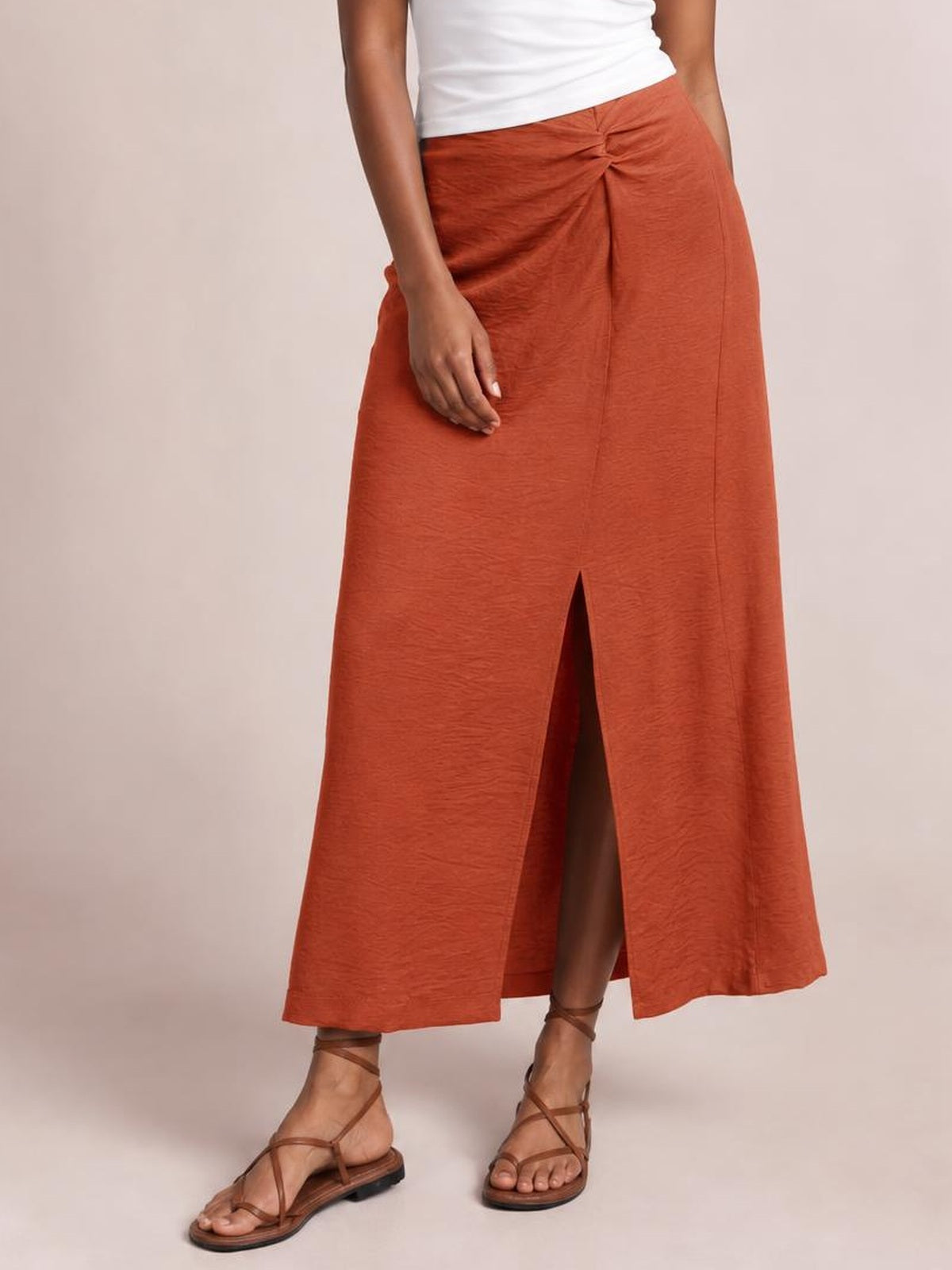 A model stands in a rust-orange flowy midi skirt with a gathered front waist, clean seams, and a modern front slit creating an easy A-line silhouette.