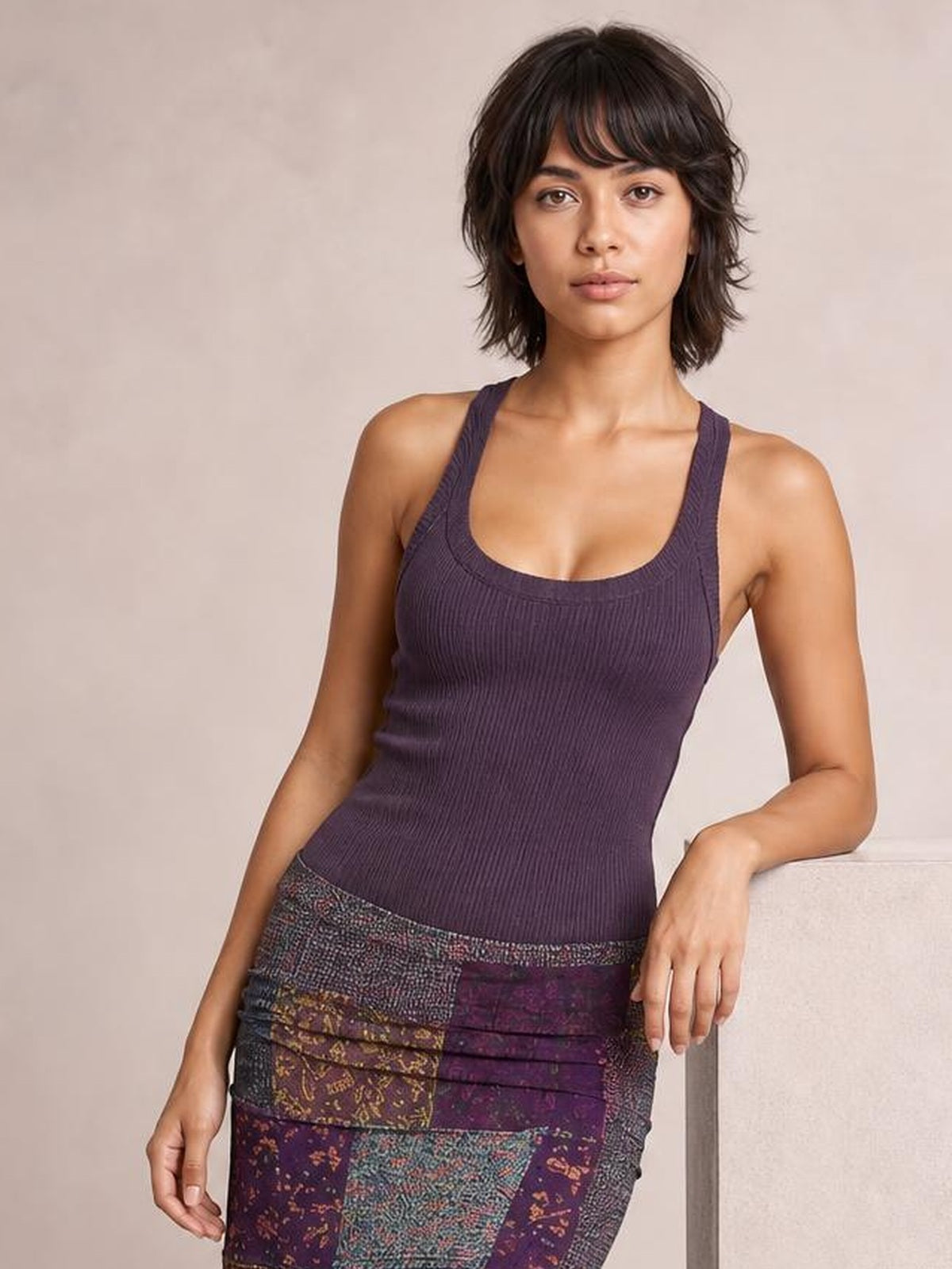 Model wears a sleeveless midi dress with a fitted purple ribbed bodice and multicolored printed patchwork skirt, posed leaning casually with one hand resting at her side.