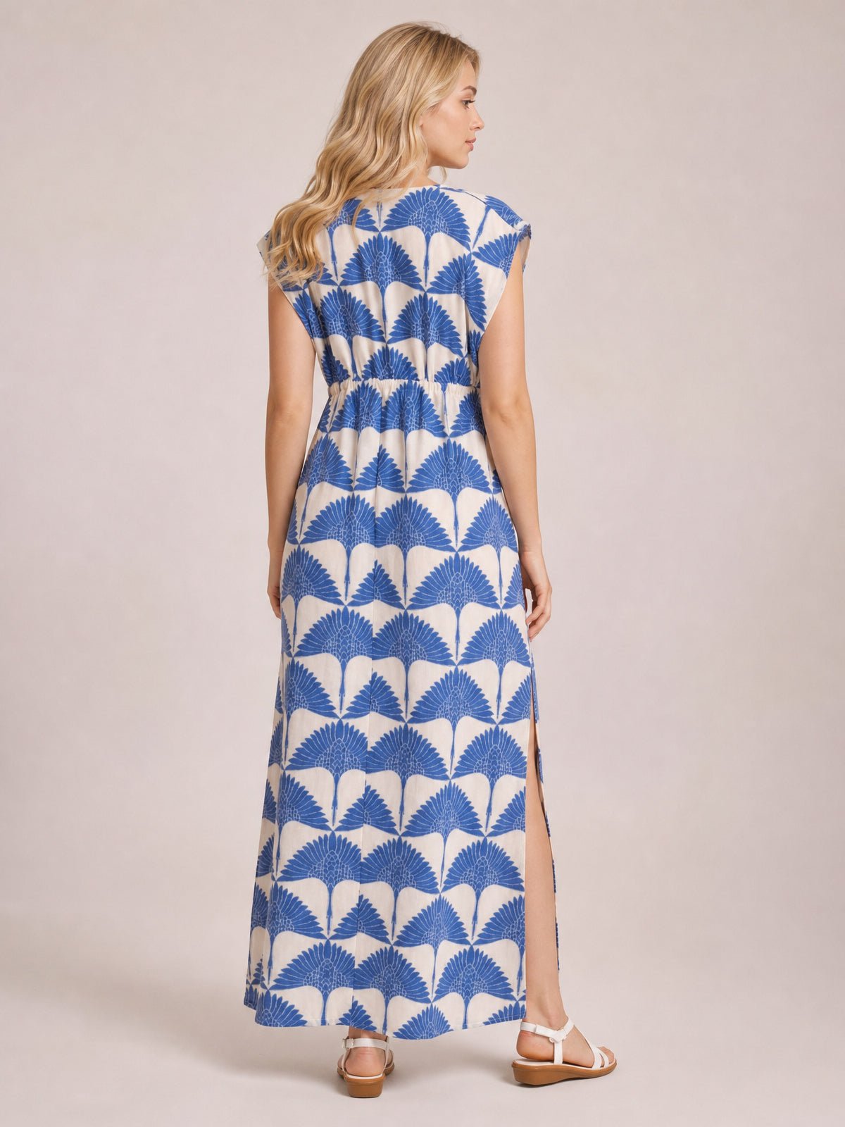 Model shown from the back in a blue-and-cream printed maxi dress with cap sleeves, a ruched waist, flowing silhouette, and side slit.