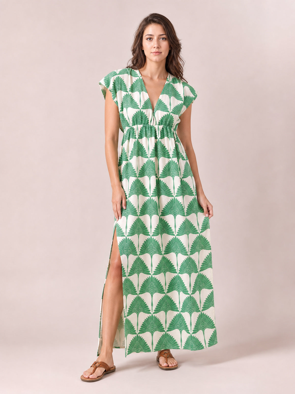 Model wears a green and ivory printed V-neck maxi dress with cap sleeves, a ruched waist, flowing silhouette, and side slit, standing in sandals.