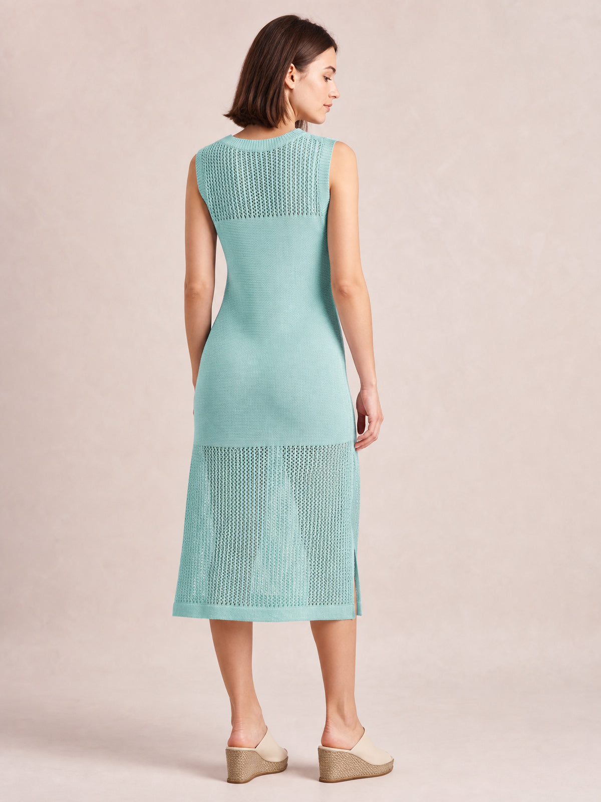 Model shown from behind in a mint sleeveless sweater dress with a round neck, fitted midi silhouette, openwork knit panels, and side slits.