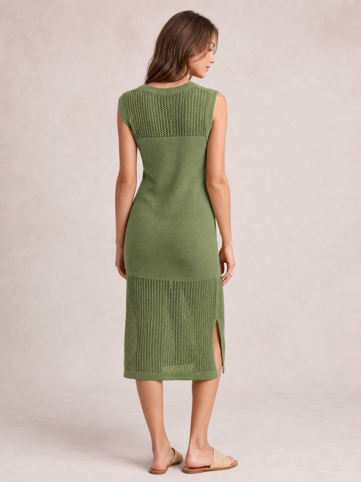 Model shown from the back wearing an olive green sleeveless sweater dress with a round neck, elongated fitted silhouette, openwork knit panels, and side slit.