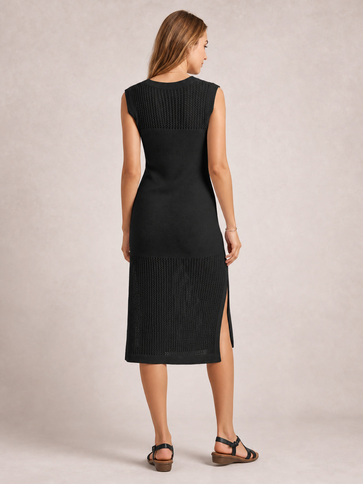 Model shown from the back wearing a black sleeveless sweater dress with a round neck, elongated silhouette, openwork knit panels, and side slit.