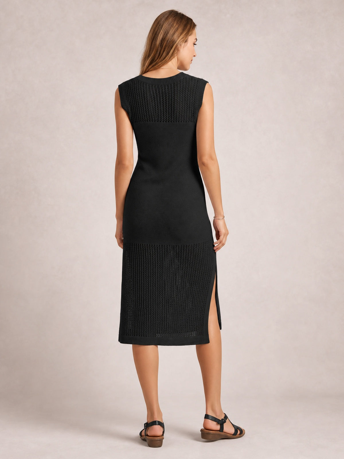 Model shown from the back wearing a black sleeveless sweater dress with a round neck, elongated silhouette, openwork knit panels, and side slit.
