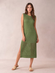 Model poses in a sleeveless olive green sweater dress with a round neck, straight midi silhouette, openwork panels, and side slit.