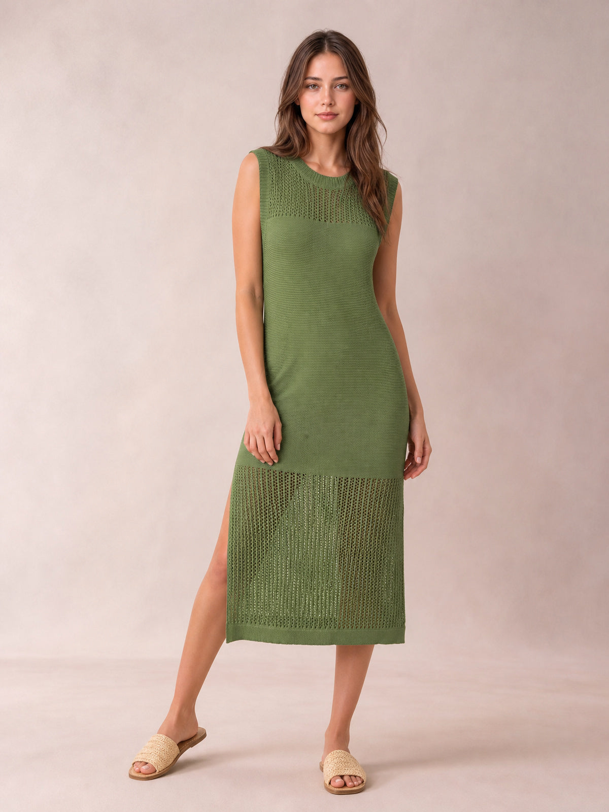 Model poses in a sleeveless olive green sweater dress with a round neck, straight midi silhouette, openwork panels, and side slit.