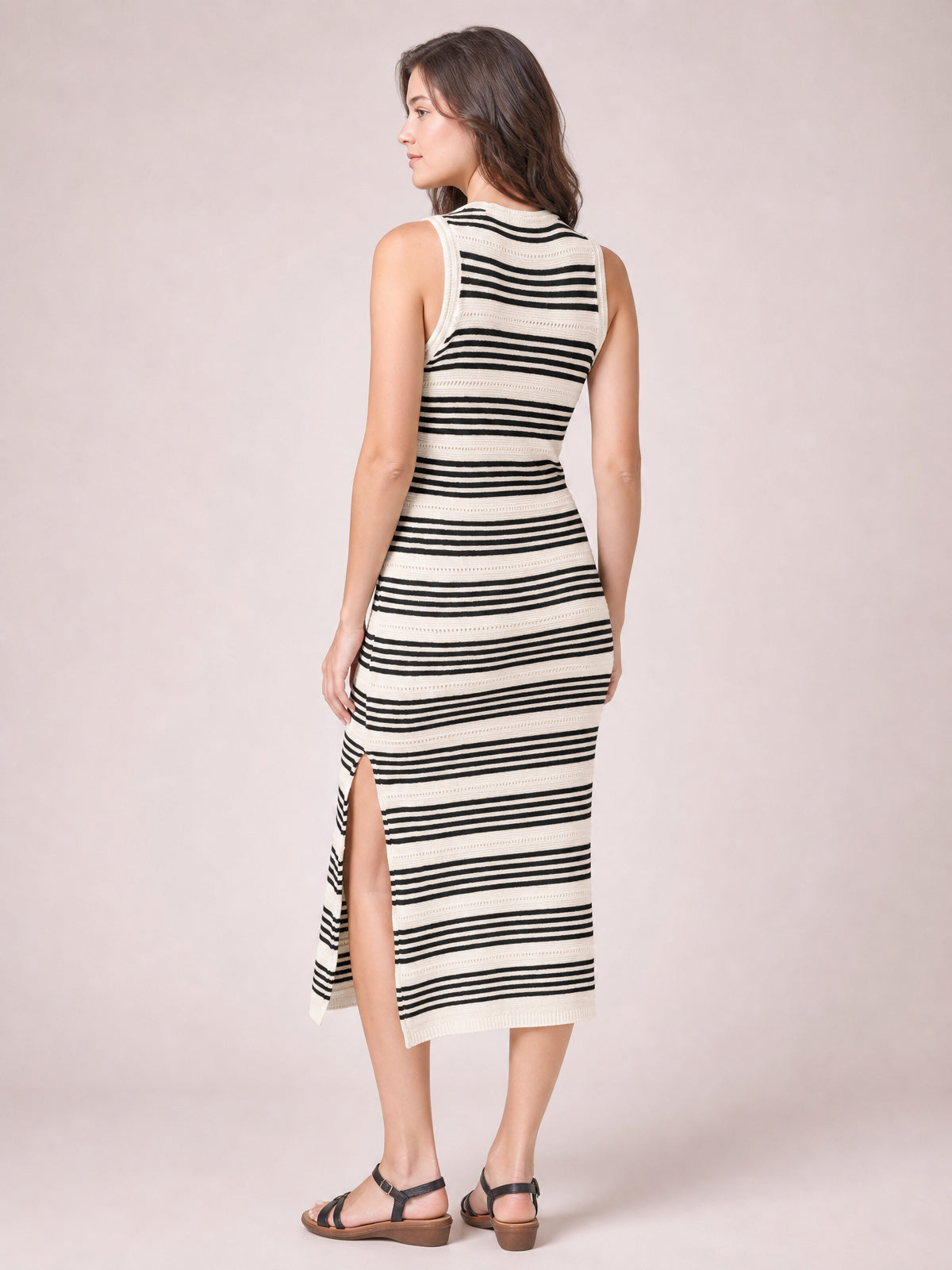Model turned away in a black-and-ivory striped sleeveless midi dress with a round neck, fitted silhouette, and high side slit.