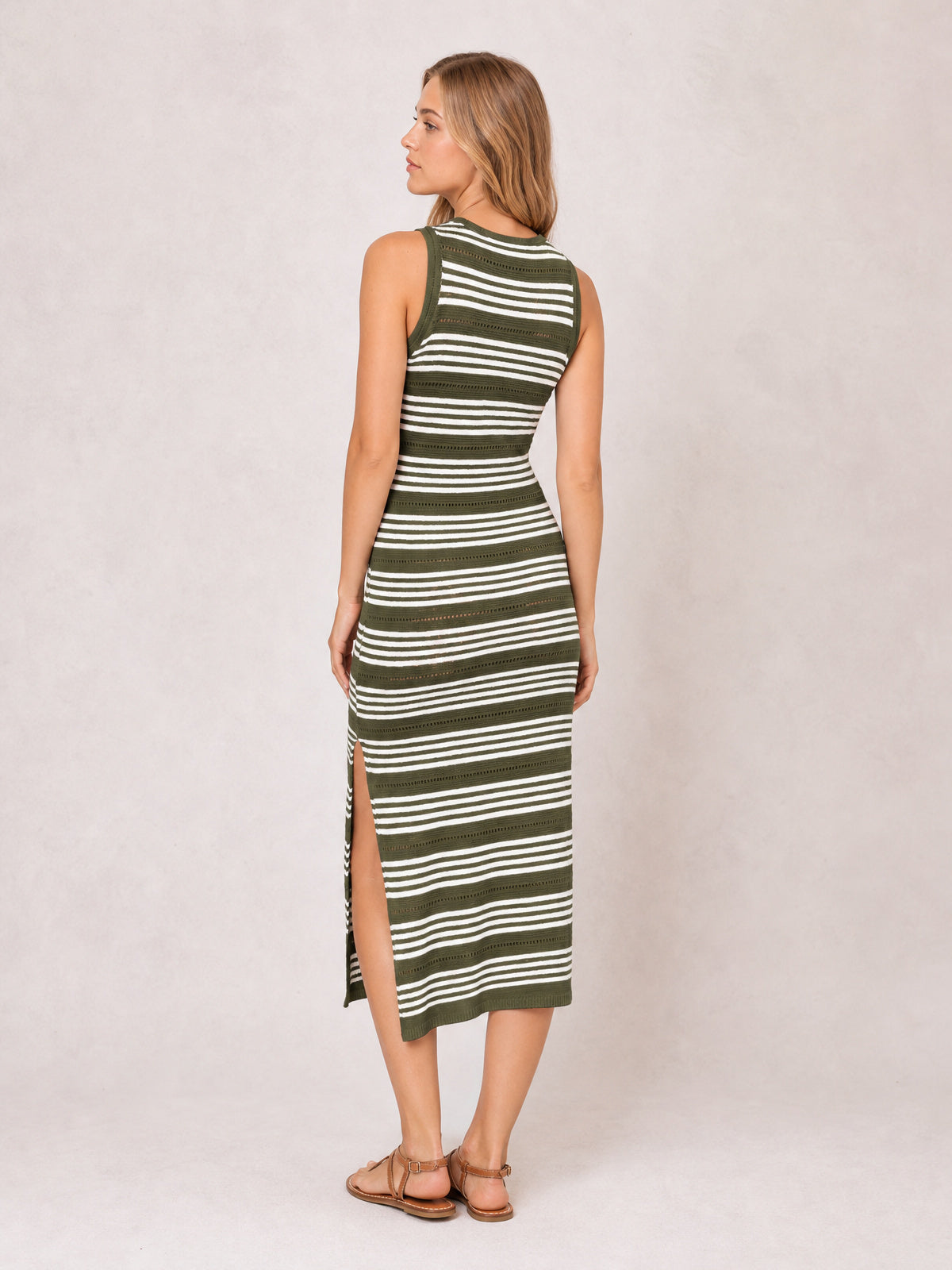 Model turned away in an olive green and white striped sleeveless midi dress with a round neckline, fitted silhouette, and side slit.