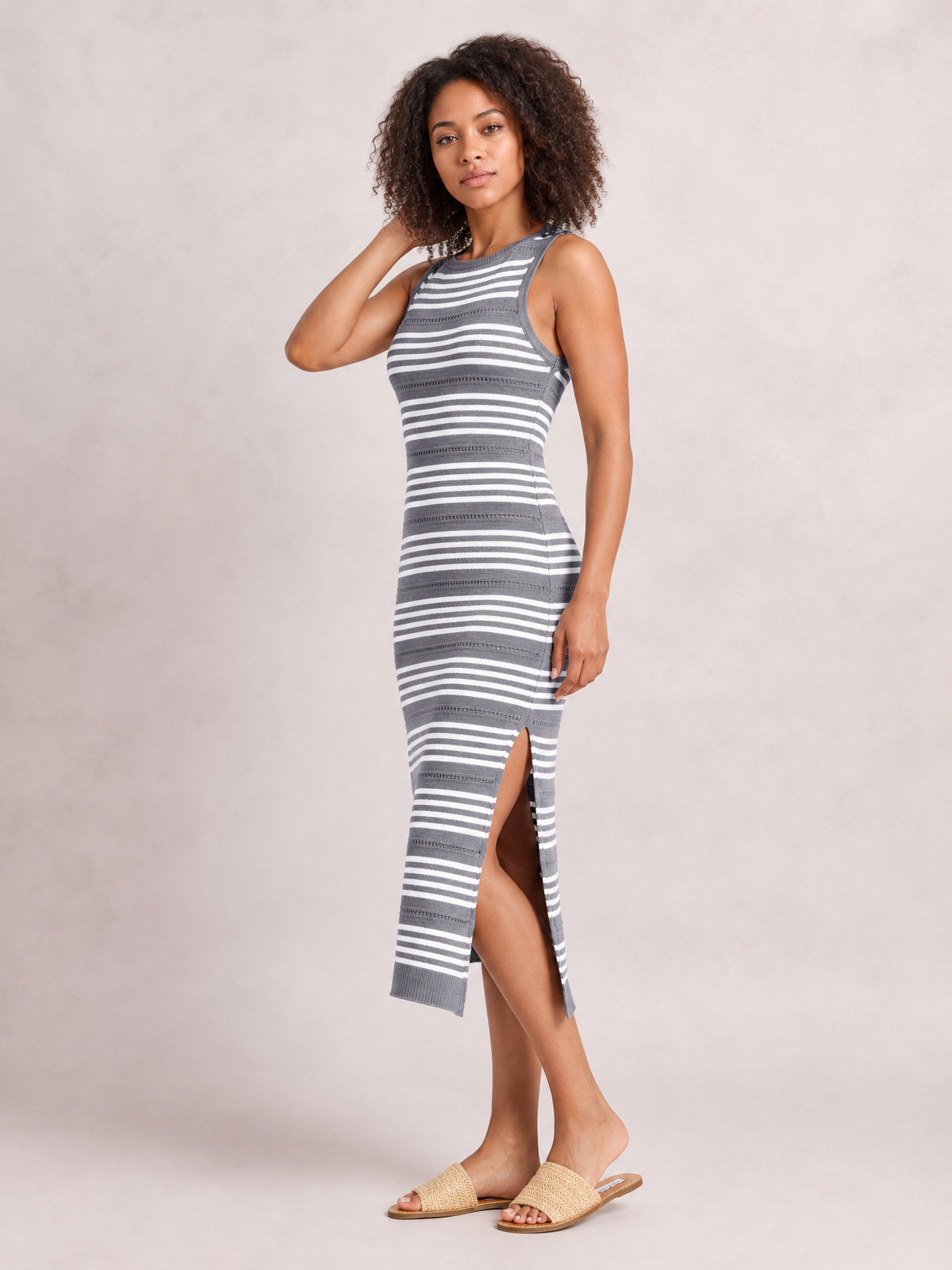 Model poses in a gray and white striped sleeveless midi dress with a round neck, fitted silhouette, and high side slit.