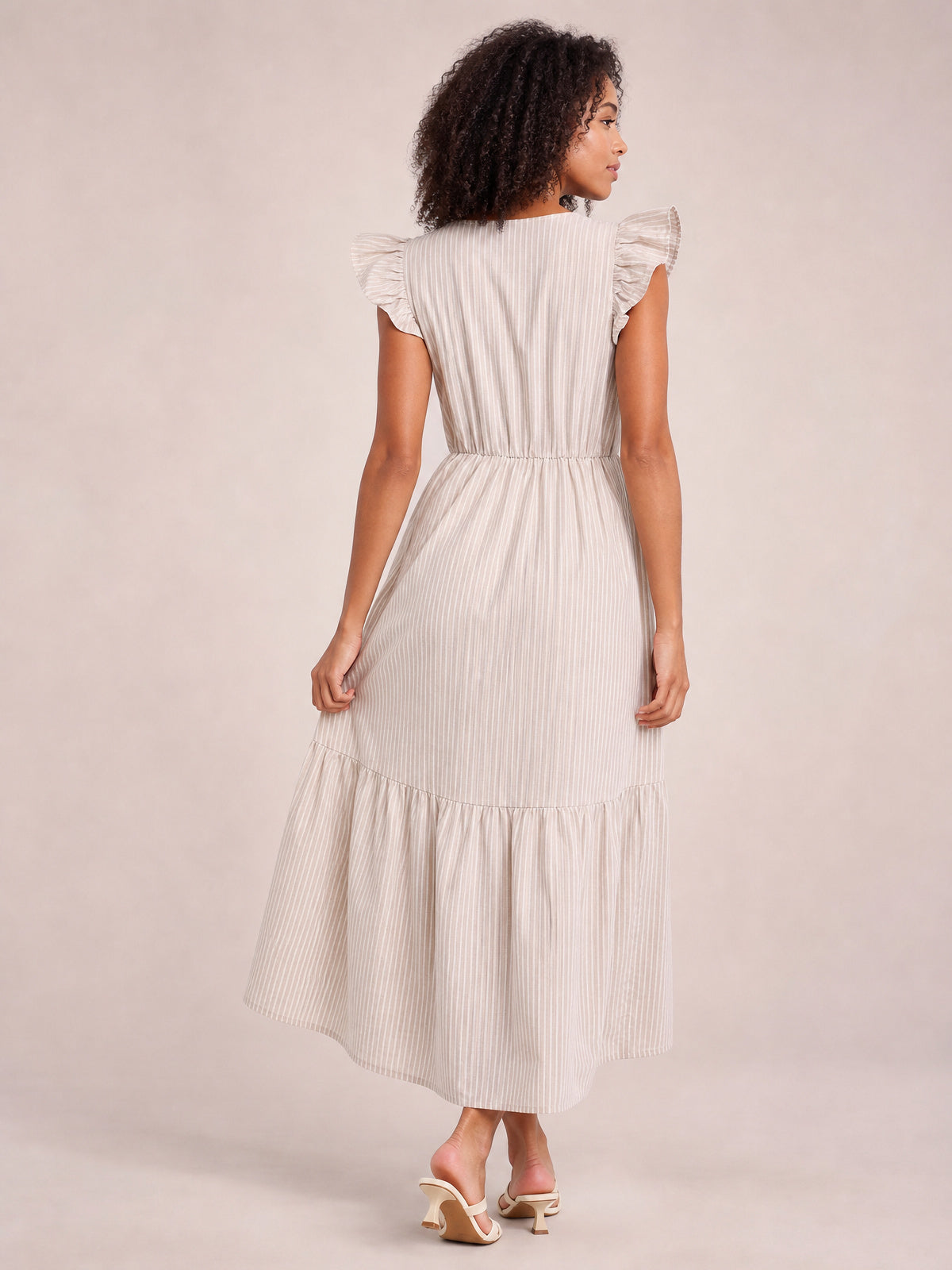 A model poses from the back in a light striped midi dress with ruffled cap sleeves, a defined waist, and a gently tiered skirt.