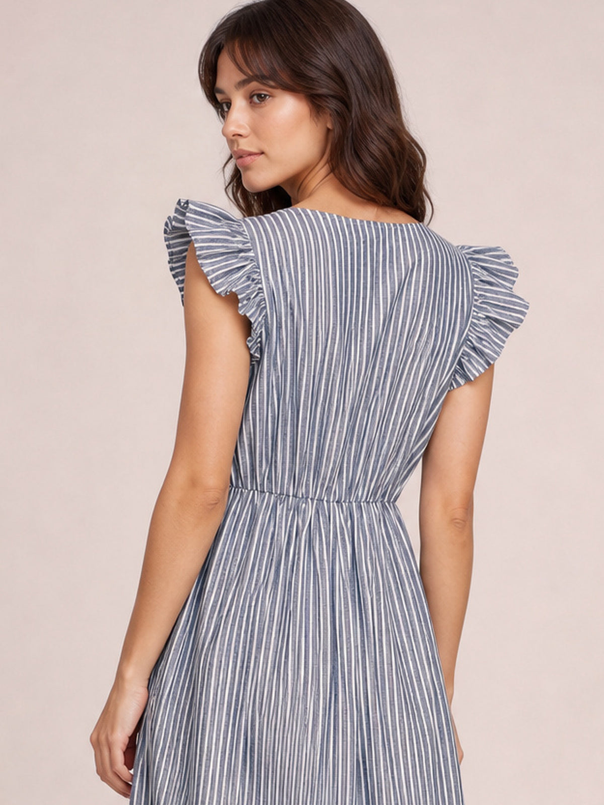 Model looks over her shoulder in a blue-and-white striped dress with ruffled cap sleeves, a defined waist, and a flowing midi-length skirt.