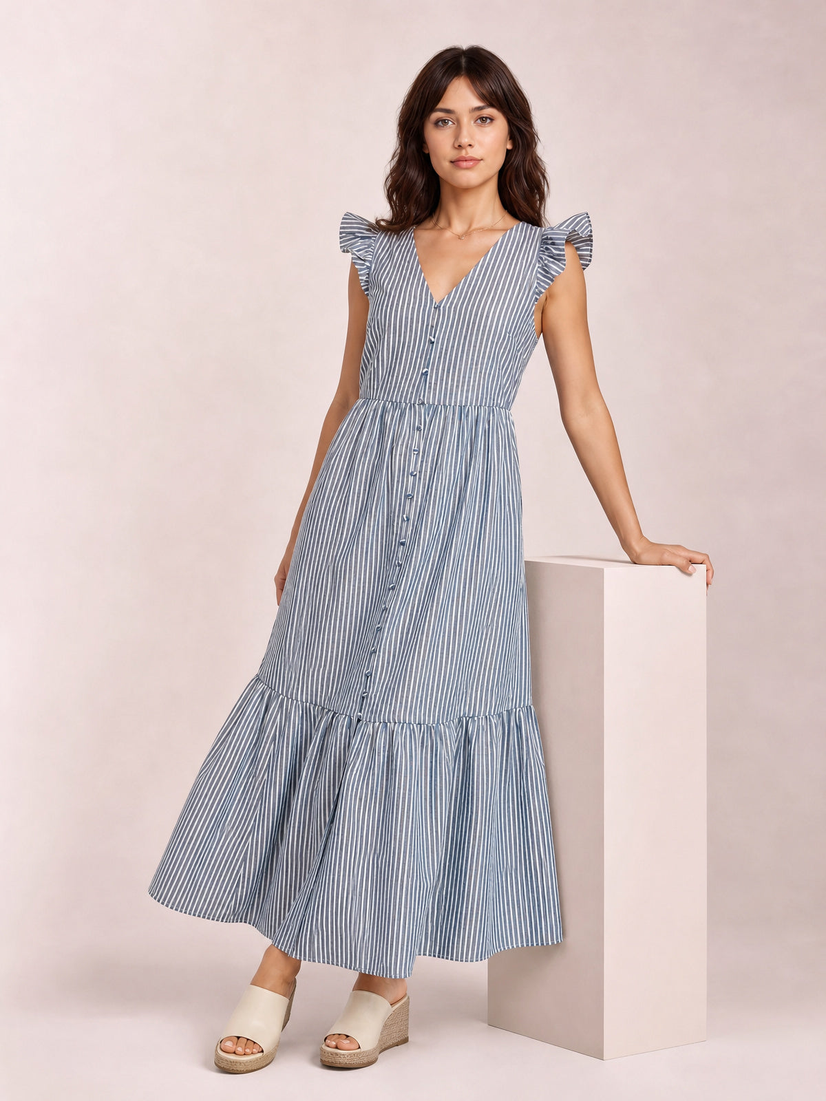 Model poses in a blue-and-white striped V-neck midi dress with ruffled cap sleeves, buttoned bodice, defined waist, and tiered skirt.