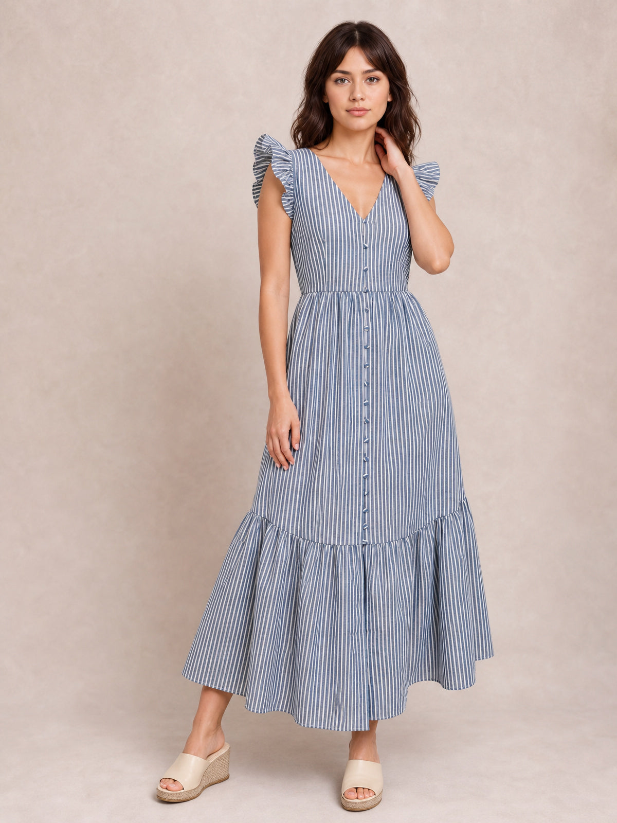 A model poses in a blue-and-white striped V-neck dress with ruffled cap sleeves, button-front bodice, defined waist, and tiered midi silhouette.