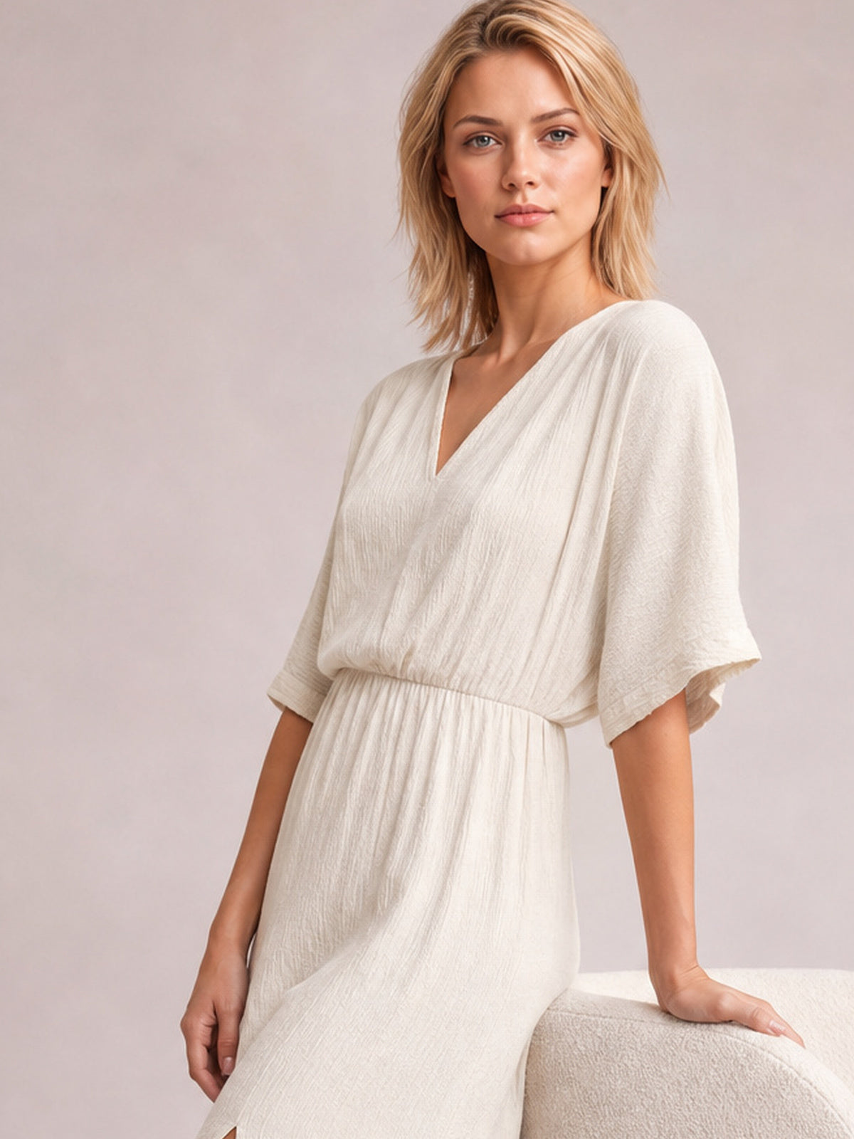 Model poses in a cream surplice midi dress with a wrap-inspired V-neckline, relaxed half sleeves, gathered waist, and softly flowing silhouette.