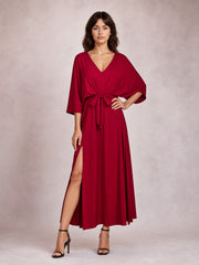 Model poses in a flowing burgundy V-neck dress with tied waist, relaxed three-quarter sleeves, flattering draped silhouette, and daring thigh-high side slit.