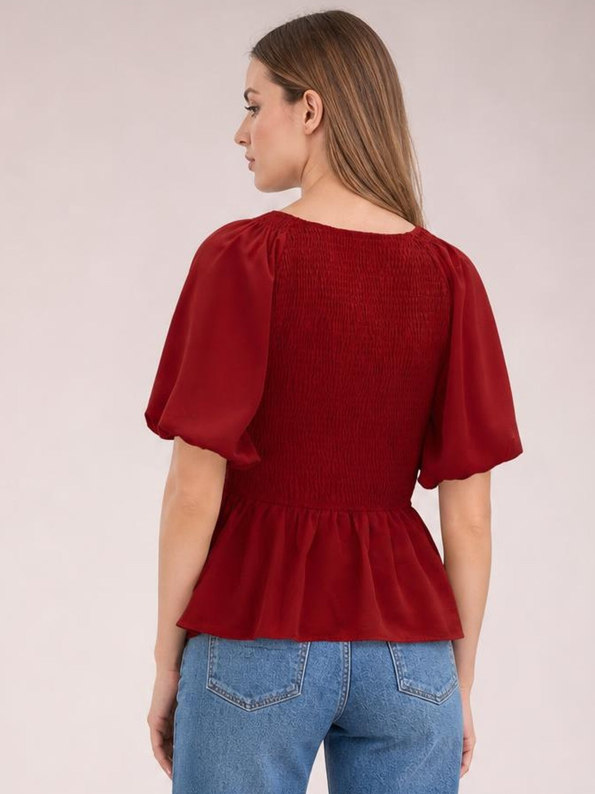 A model stands in a deep red peplum blouse with a smocked back, short balloon puff sleeves, a gathered waist, and a flared hem.
