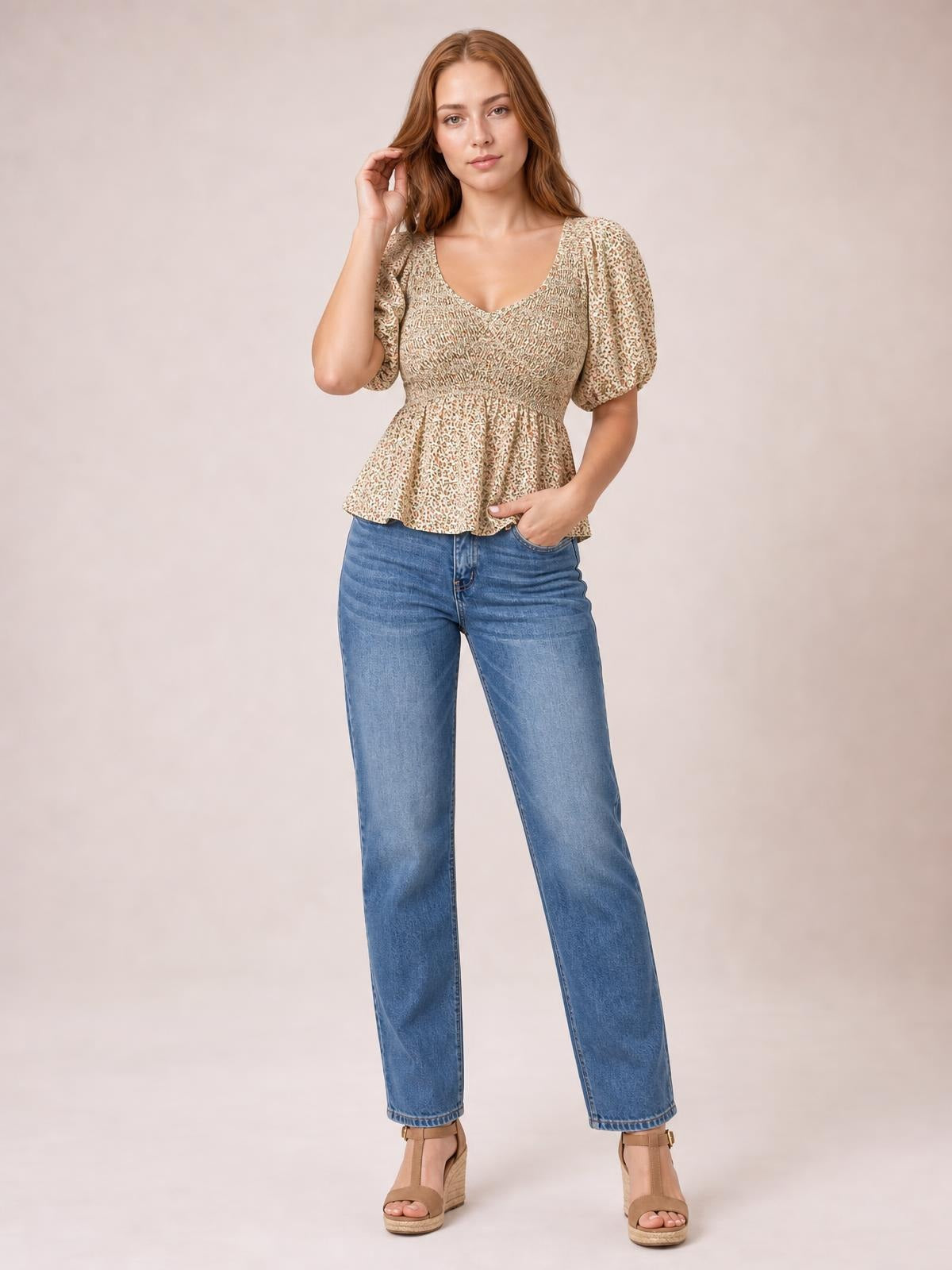 Model poses in a beige floral-print smocked peplum blouse with a V-neck, short balloon puff sleeves, fitted bodice, and flared hem.