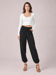 A model poses in black high-rise smocked joggers with side pockets, a relaxed silhouette, and elasticized cuffs tapering at the ankles.