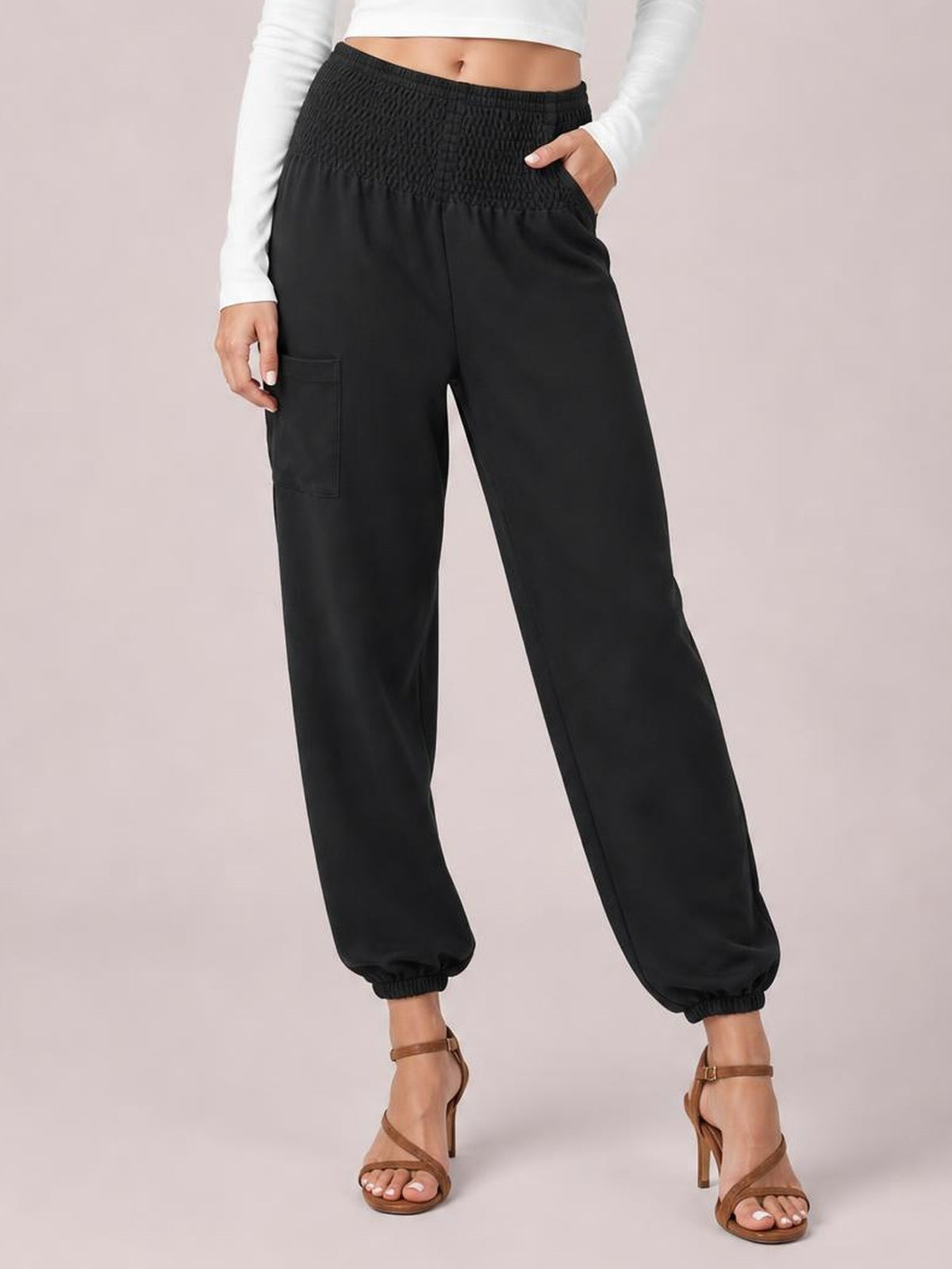 Model poses in black smocked high-rise joggers with side and cargo-style pockets, relaxed straight-leg silhouette, and elasticized ankle cuffs.