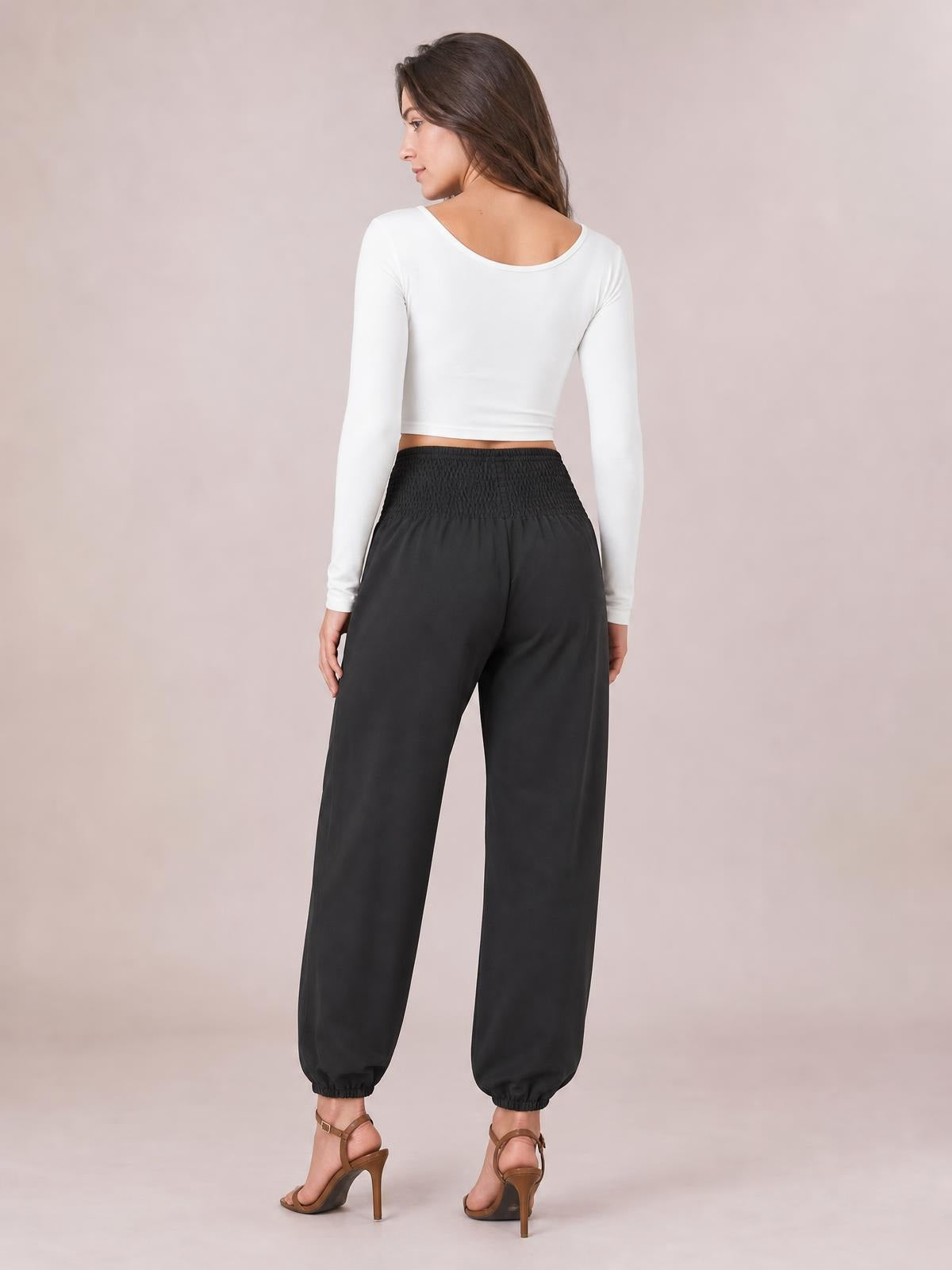 A model viewed from behind wears black smocked high-rise joggers with a relaxed silhouette, wide legs, and gathered elastic cuffs.