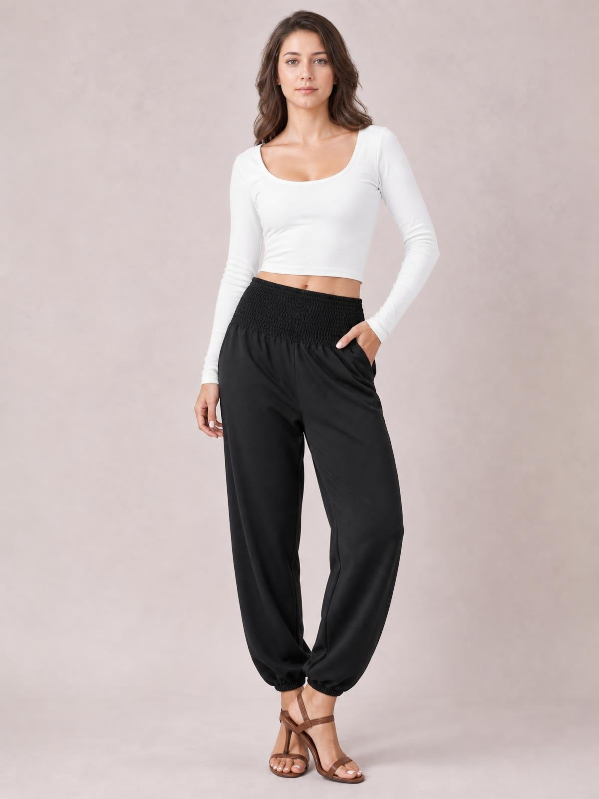 Model poses in black high-rise smocked joggers with side pockets, a relaxed wide-leg silhouette, and elasticized ankle cuffs.