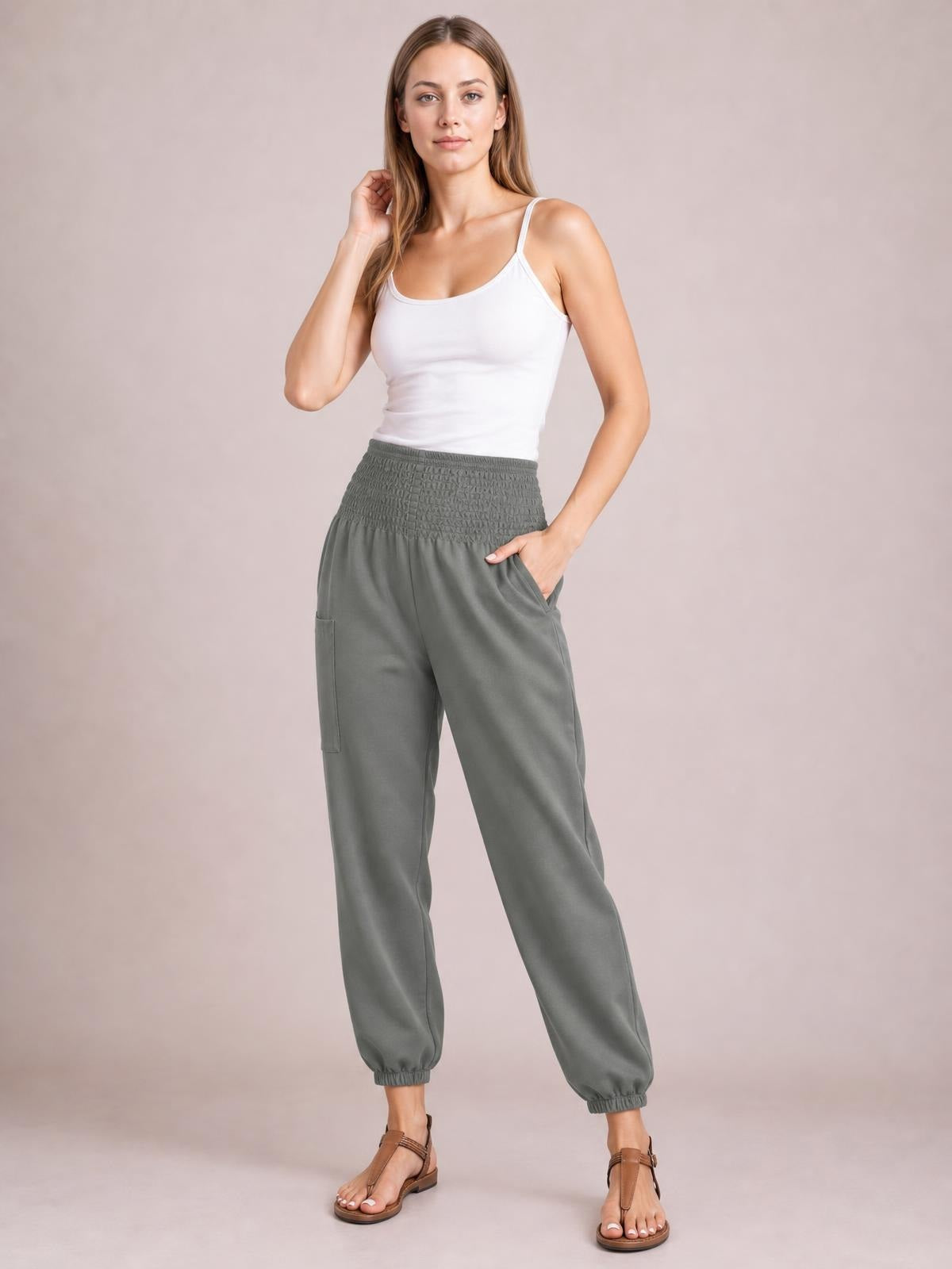 Model wearing gray high-rise smocked joggers with side and cargo pockets, relaxed straight-leg silhouette, and elasticized ankle cuffs.