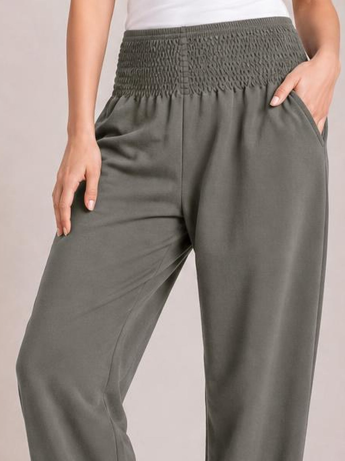 A cropped model wears charcoal gray high-rise joggers with a smocked waistband, relaxed wide-leg silhouette, and side pockets, posing with hands near the hips.