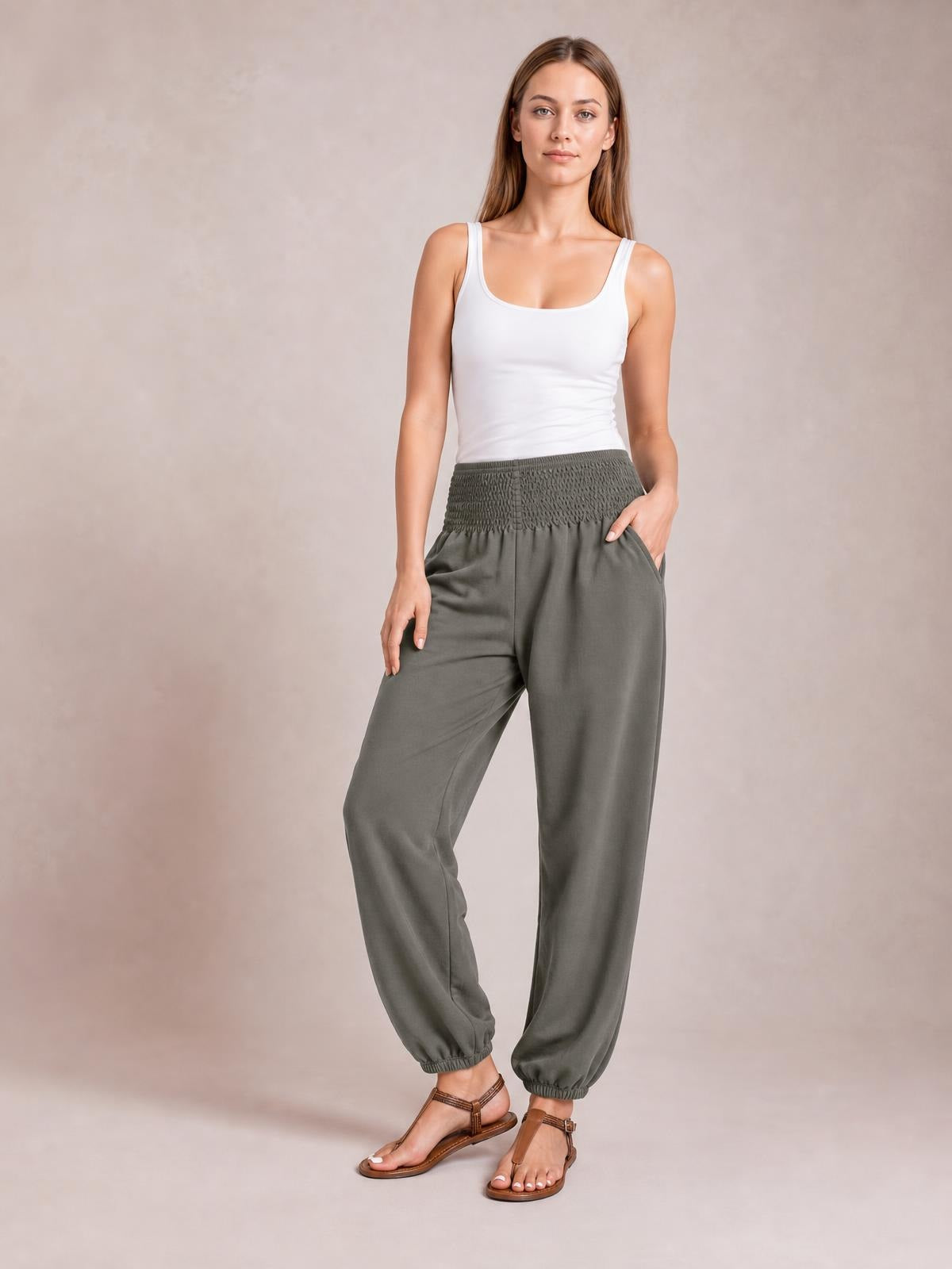 Model poses in olive-gray high-rise smocked joggers with side pockets, a relaxed wide-leg silhouette, and elasticized cuffs.