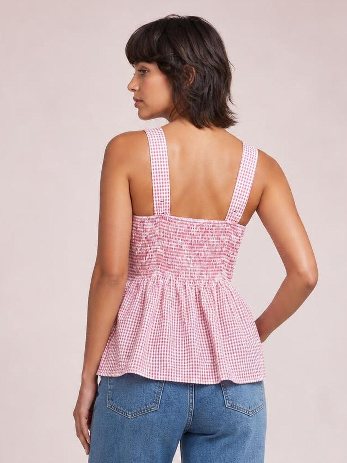 Model shown from behind in a pink-and-white plaid smocked tank with wide straps, a fitted bodice, and a flared peplum silhouette.